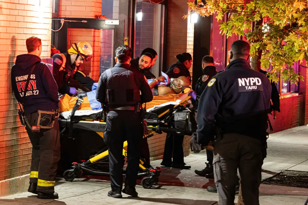 Police and emergency responders transport an injured person on a stretcher from a shooting scene.