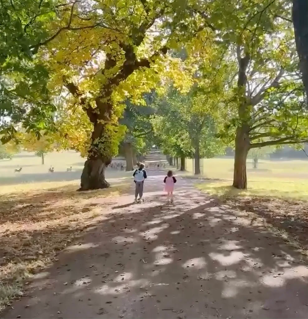 Prince Archie, on a scooter, and Princess Lilibet walking along a park path.