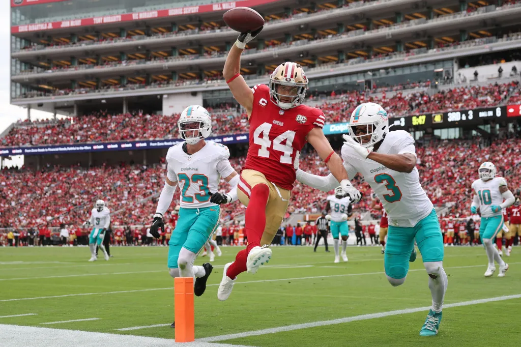 Kyle Juszczyk of the San Francisco 49ers leaps into the end zone past defenders from the Miami Dolphins to score a touchdown.
