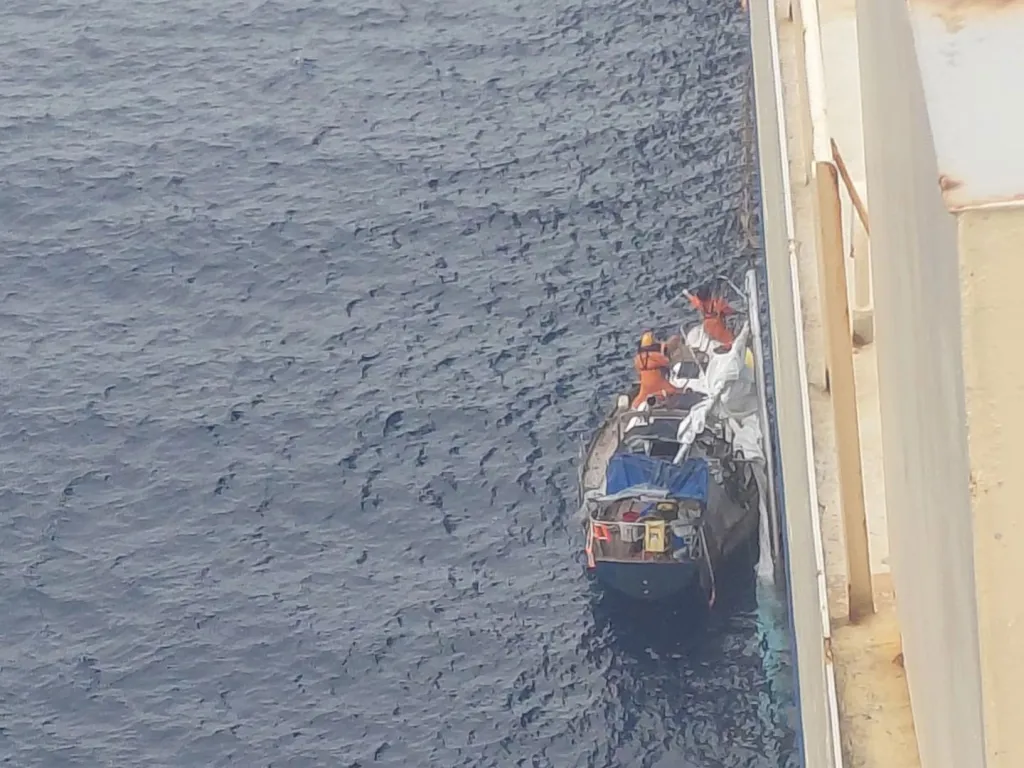 A small sailboat alongside a larger vessel during a rescue operation at sea.