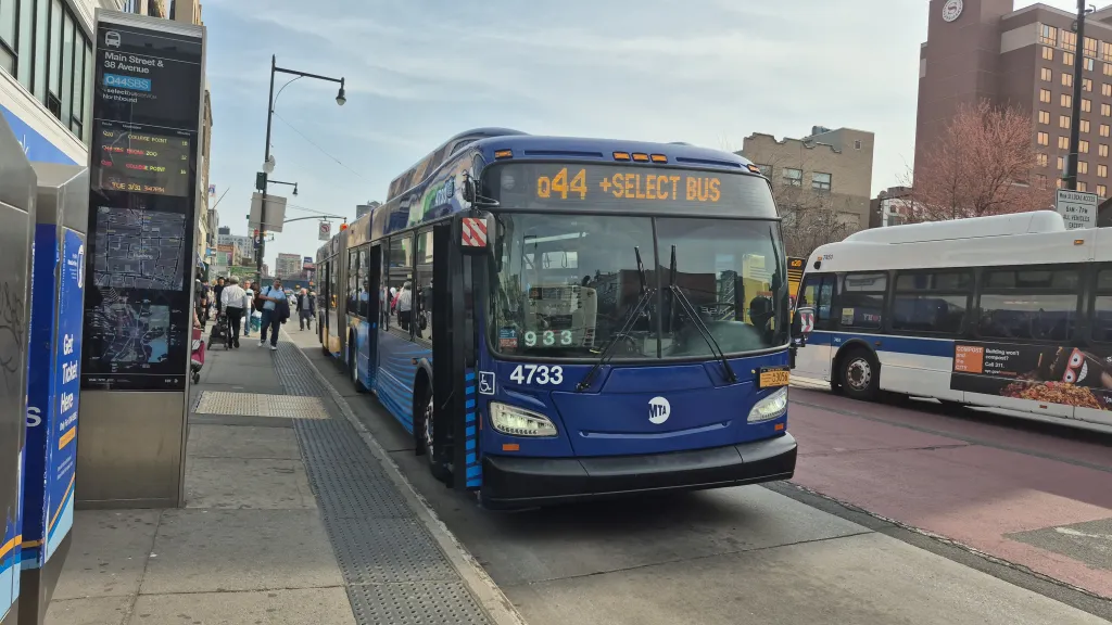 An MTA bus labeled Q44 +Select Bus at a street stop with passengers nearby.