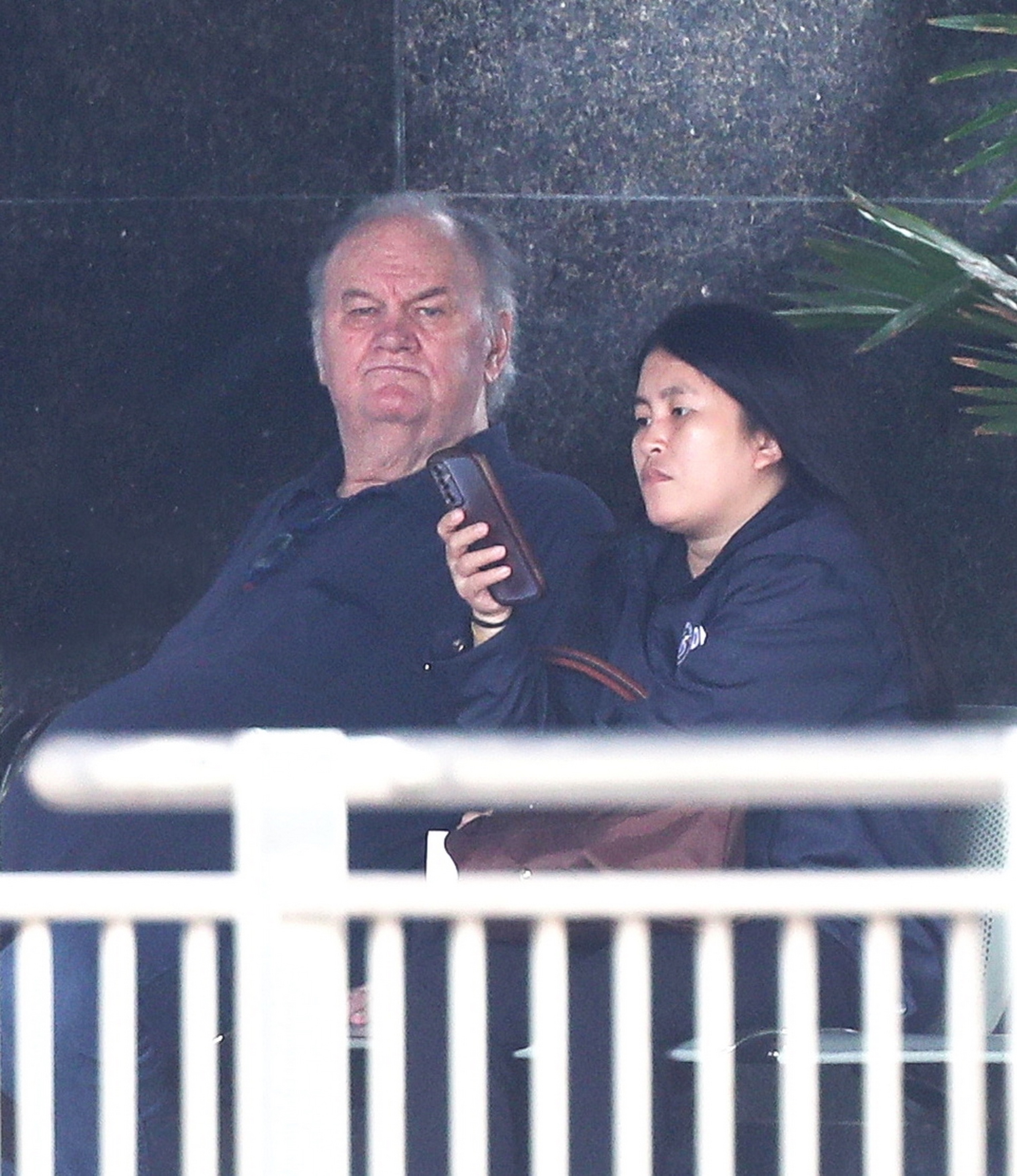 Thomas Markle sits next to a woman in a dark jacket holding a phone.