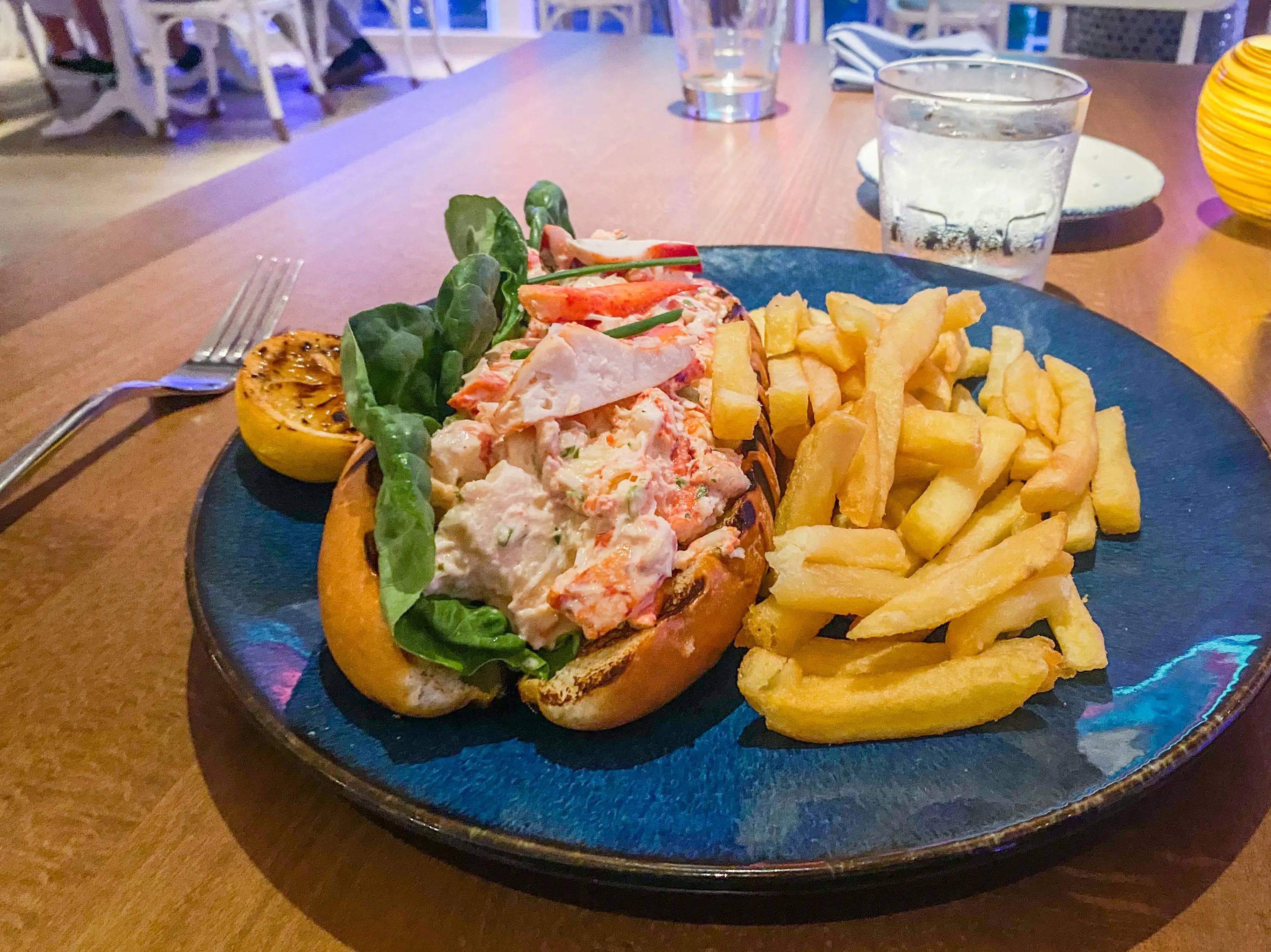 Lobster roll with fries on a blue plate at Hooked