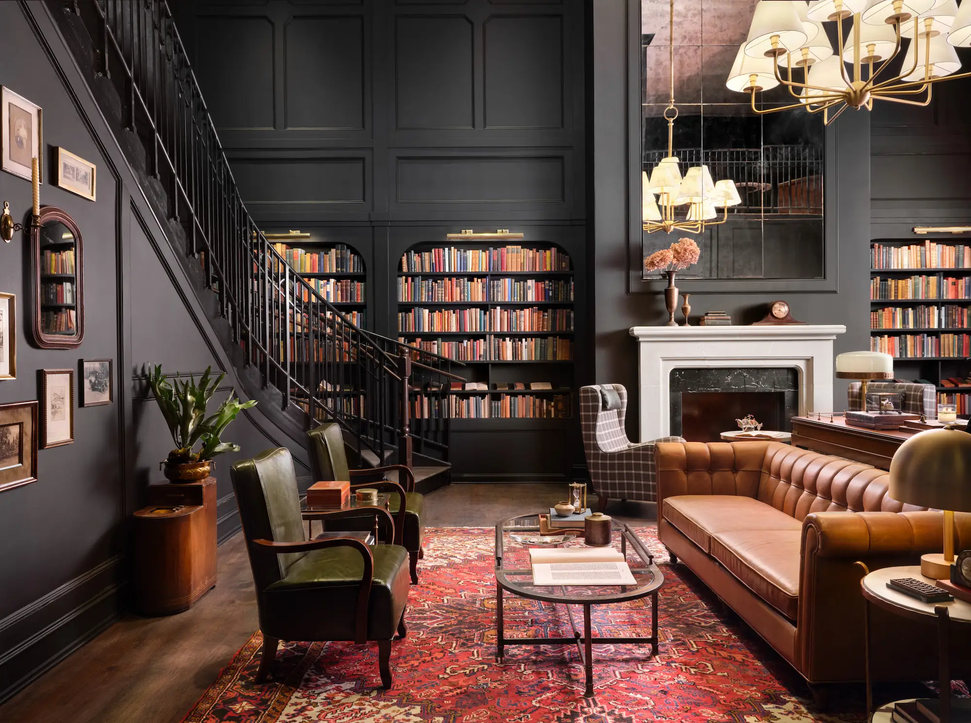 A library with a large mirror, a white fireplace, built-in bookshelves, and a sweeping staircase.