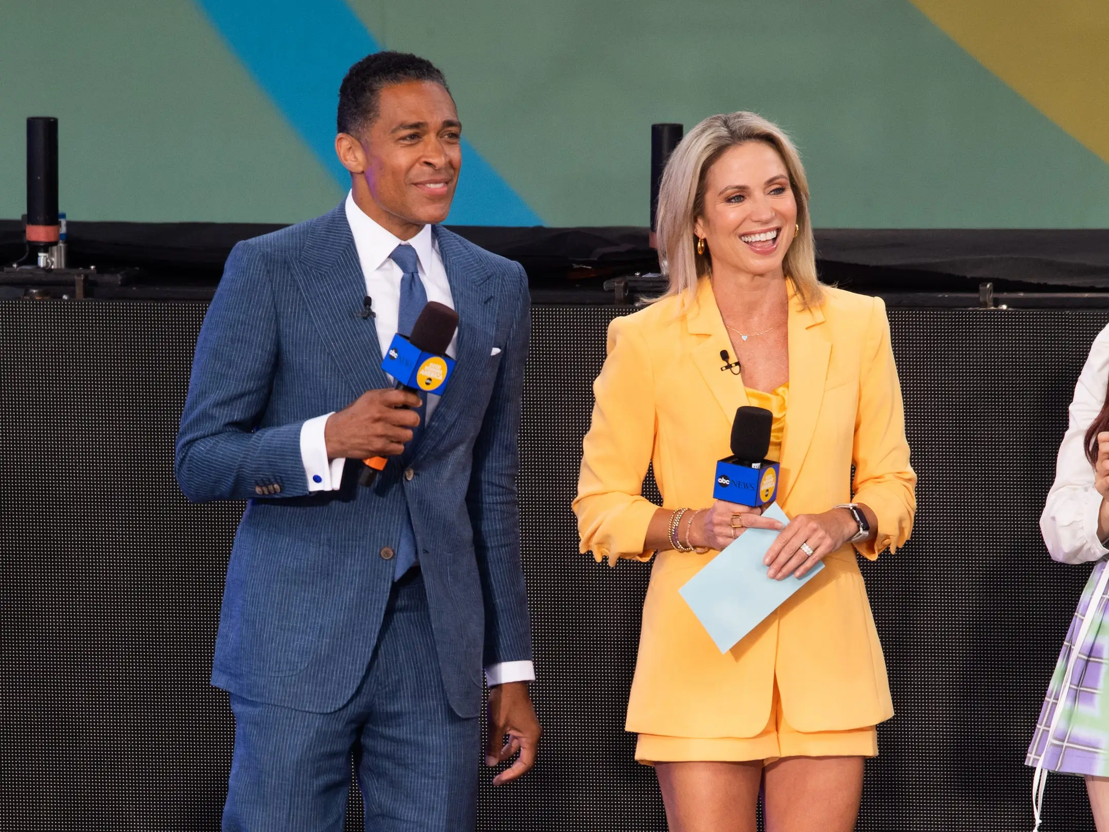 T.J. Holmes, in a blue suit, smiles while standing next to fellow 