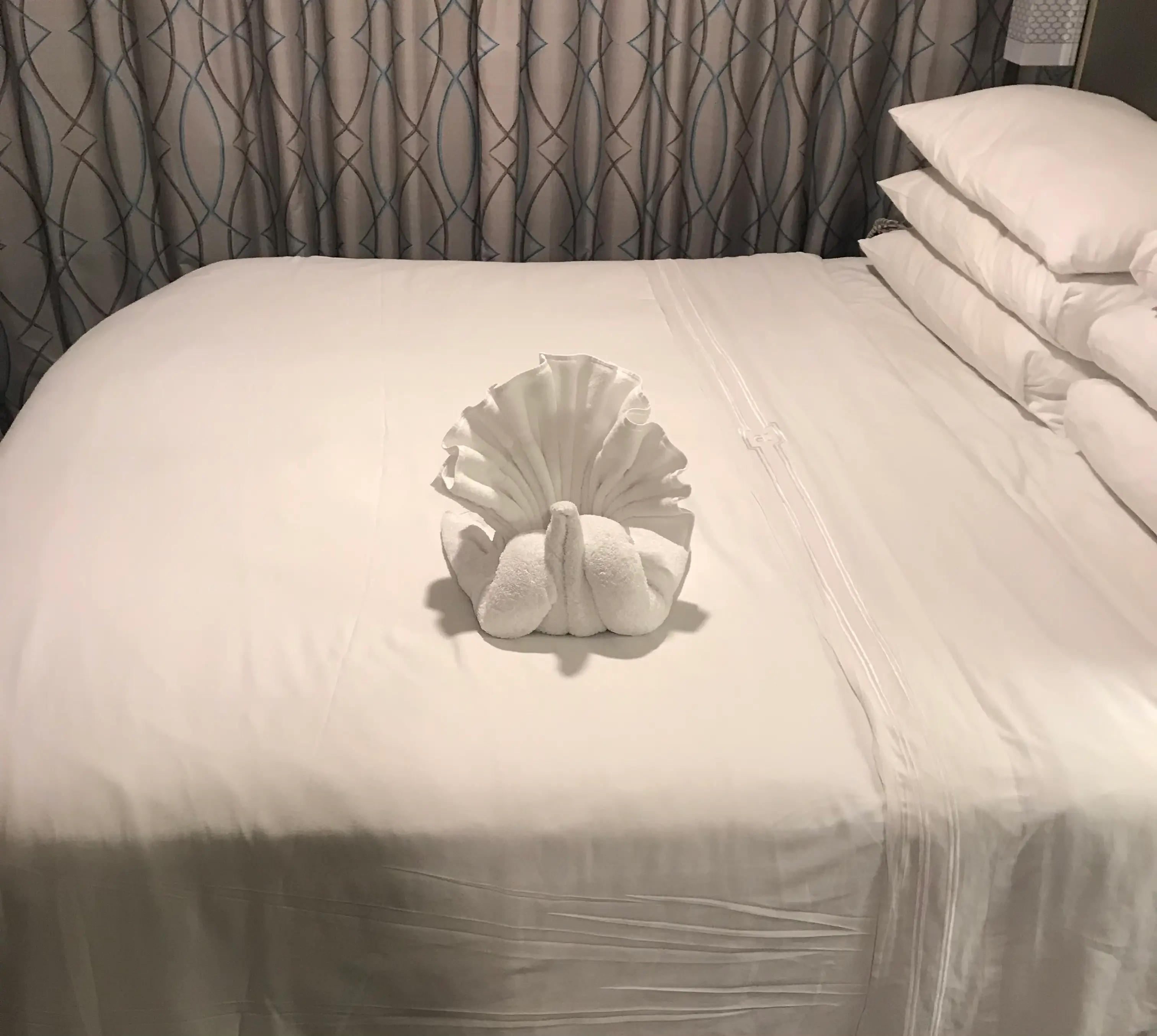towel folded like a swan on a made bed in a cruise cabin