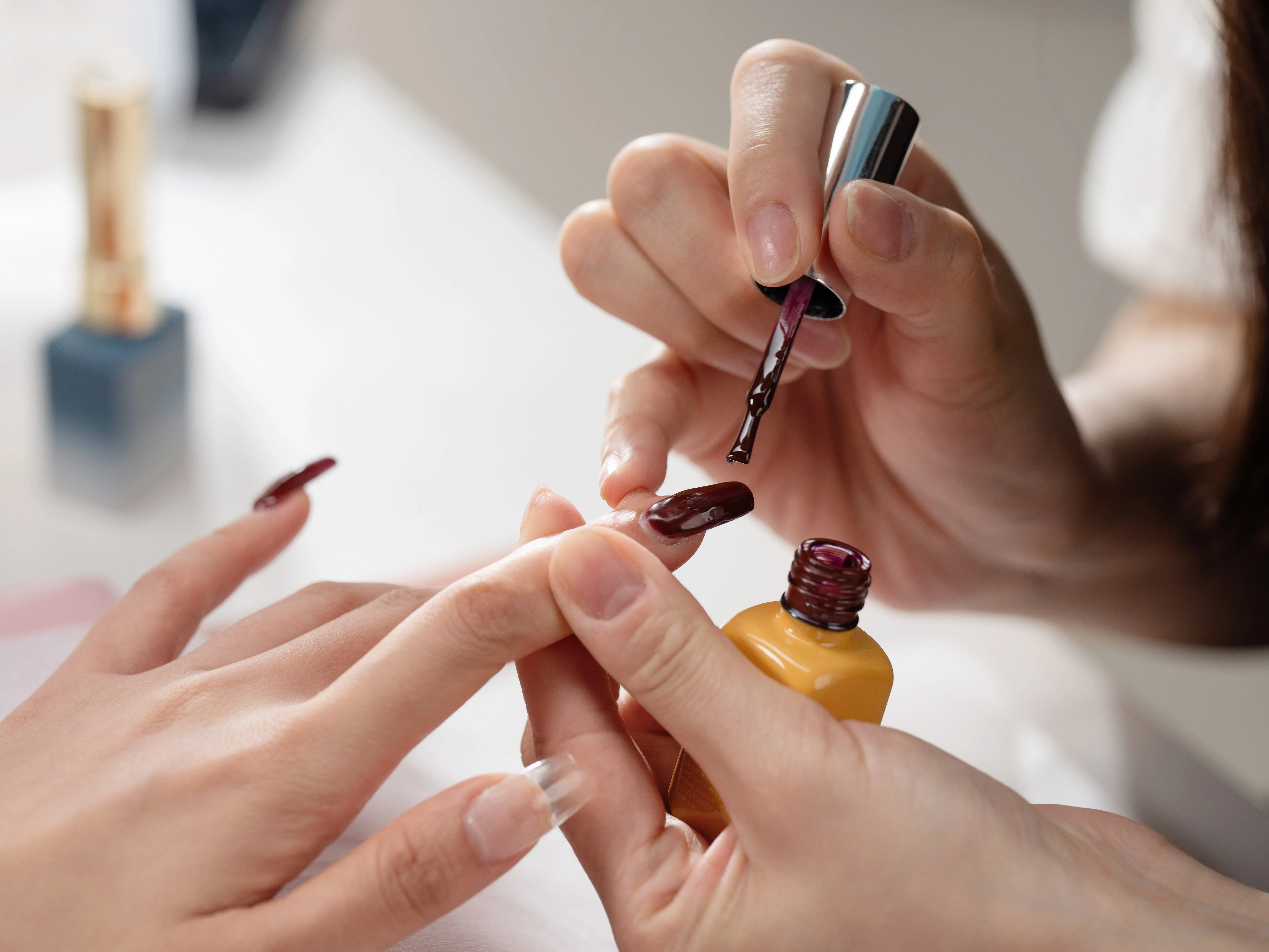 A nail technician painting someone's nails a deep purple color.
