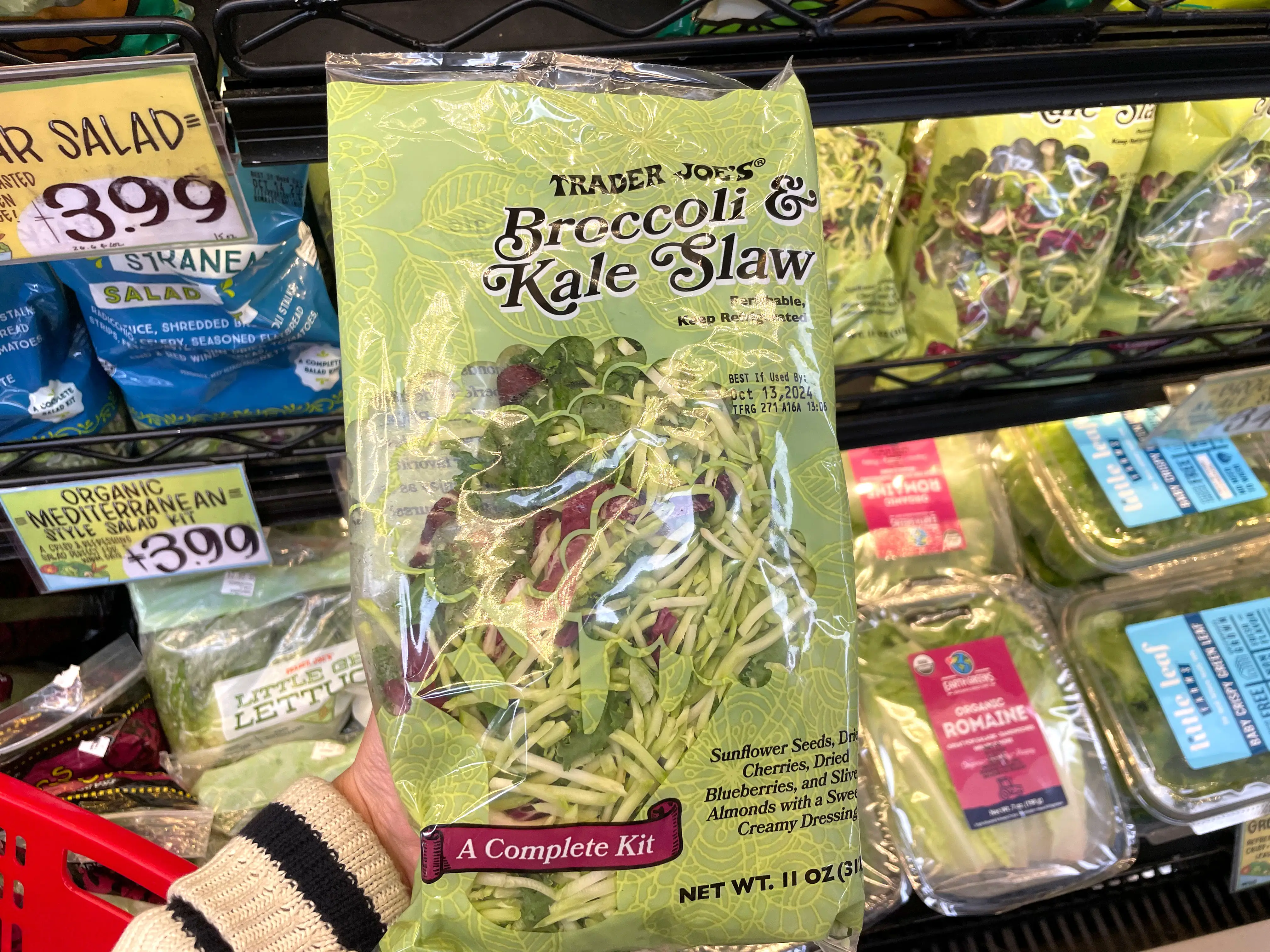 A hand holding a bag of Trader Joe's broccoli-and-kale slaw.