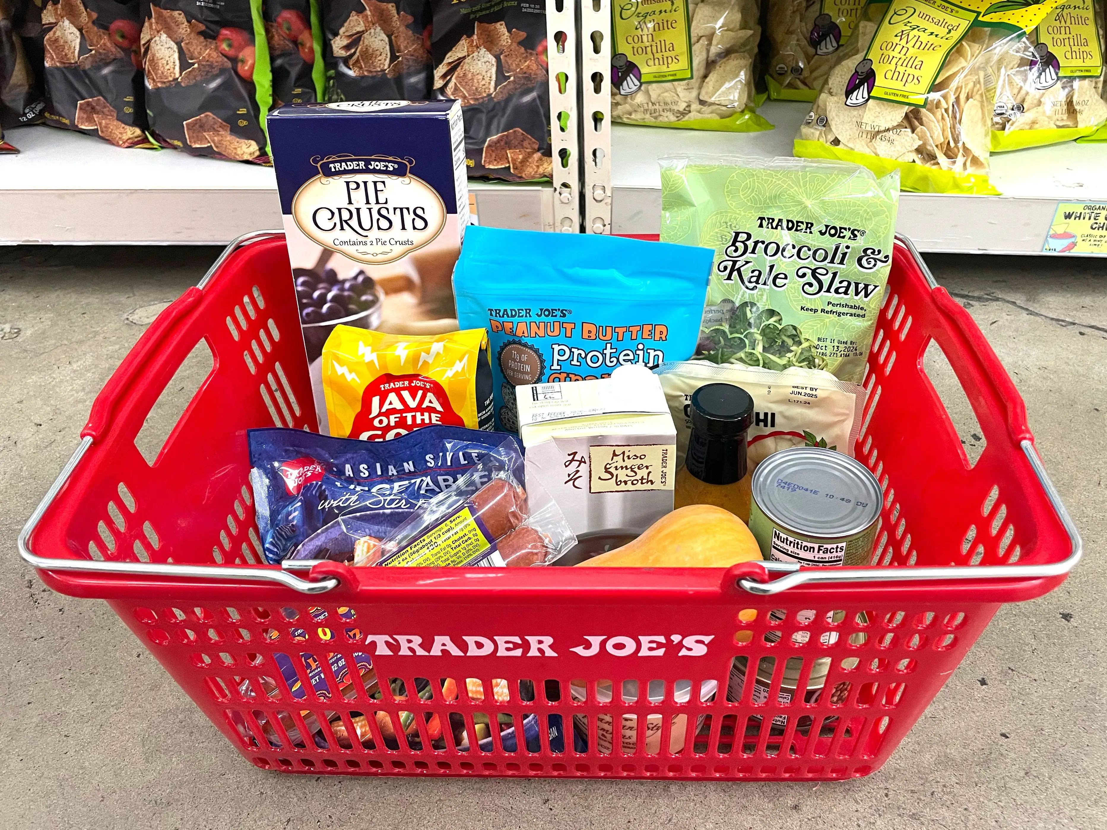 A red Trader Joe's basket on the floor, filled with different products.