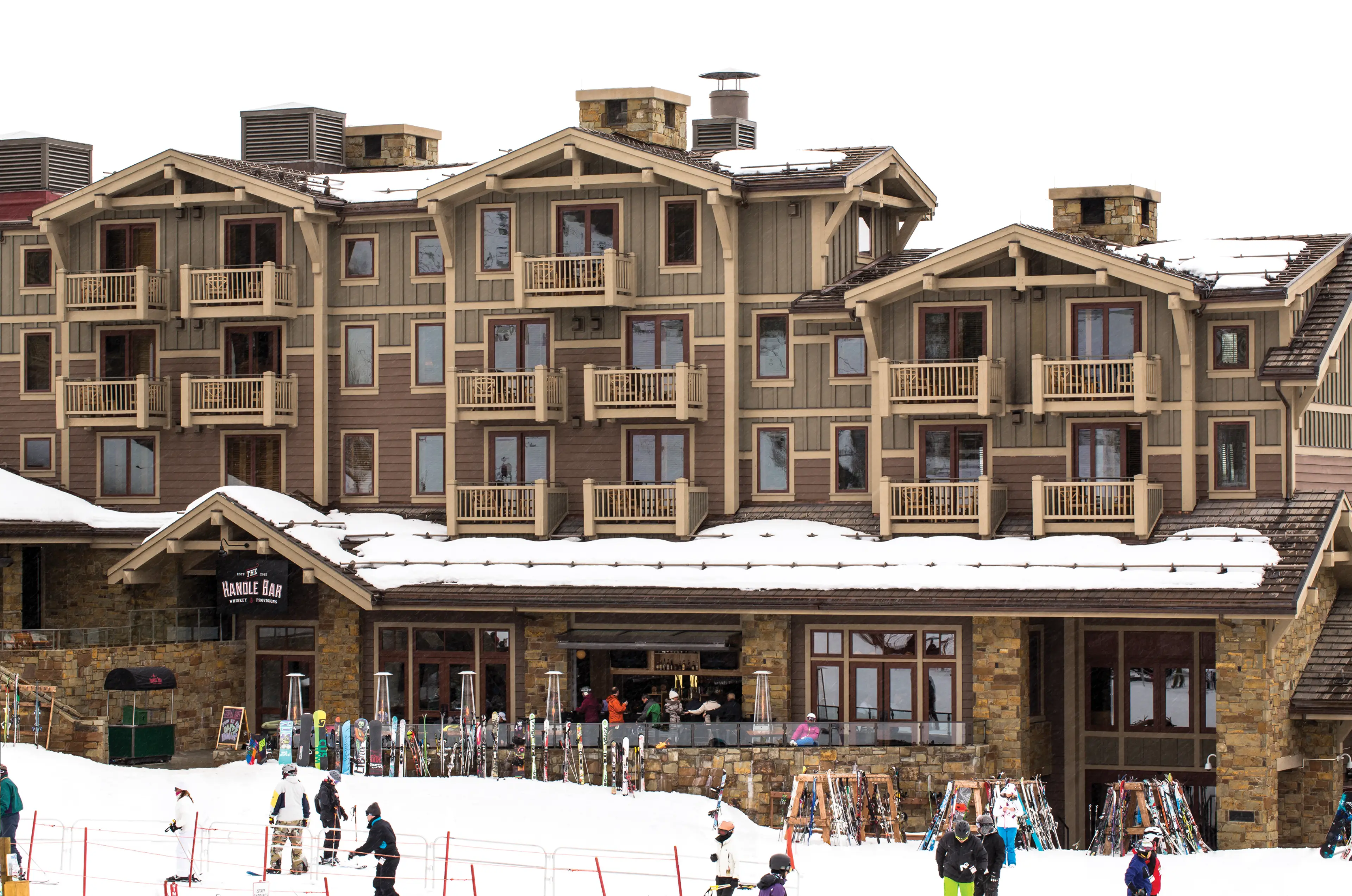 The outside of a cabin like hotel with people skiing in the snow in front of it.