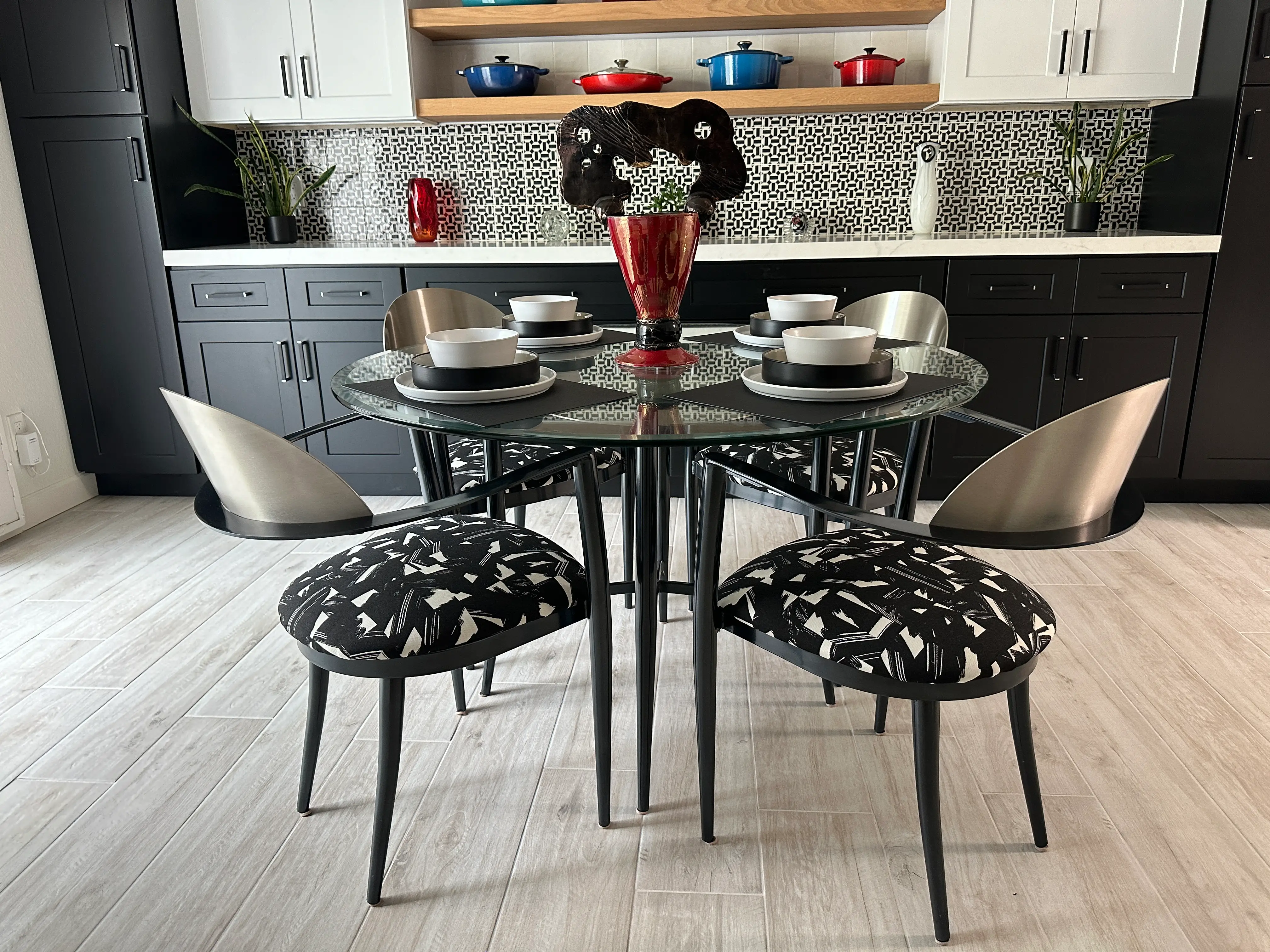 Black and metal dining chairs with patterned black and white fabric around a glass-topped table with black metal legs
