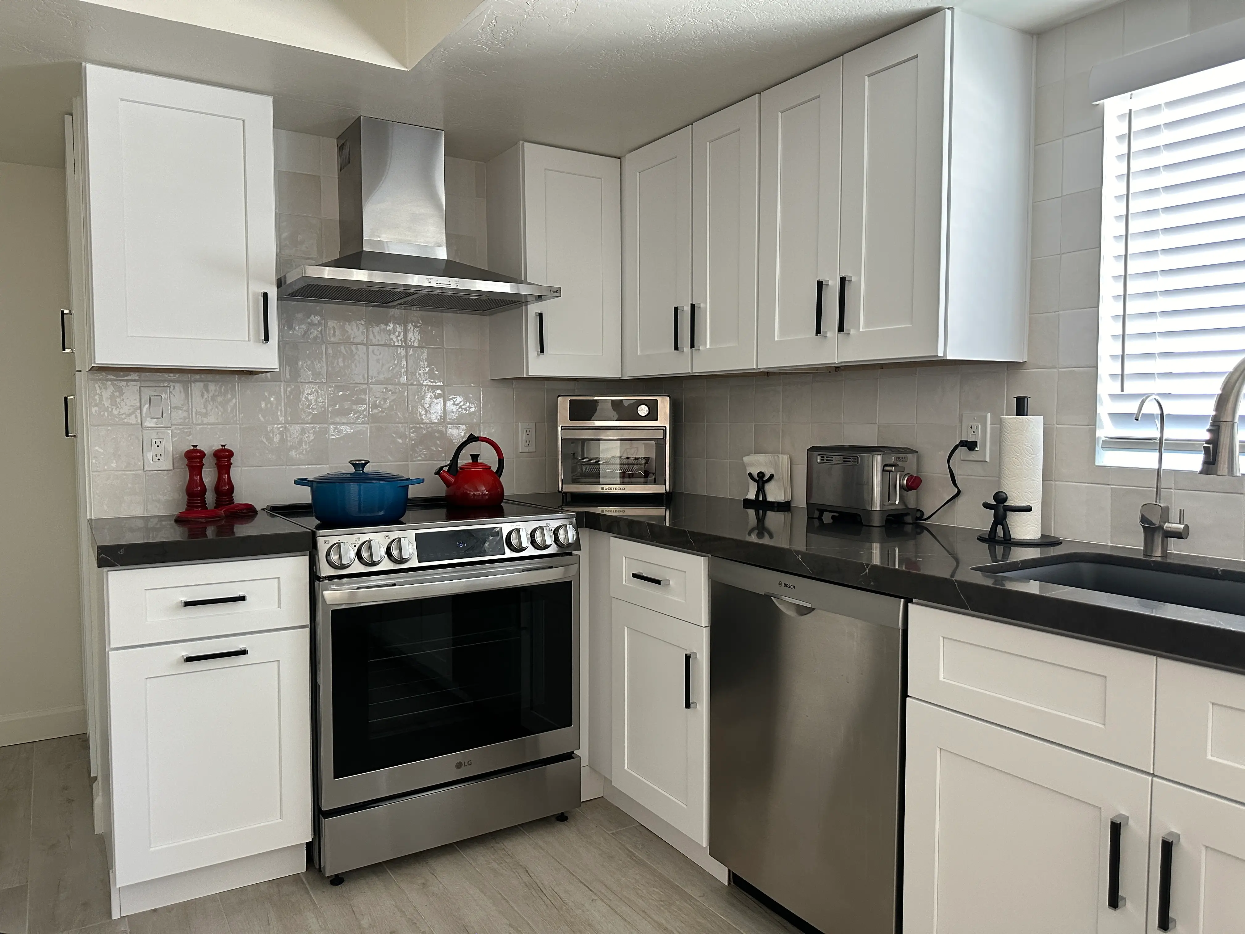 White backsplash with white upper cabinets with black hardware and black countertops with stainless steel appliances