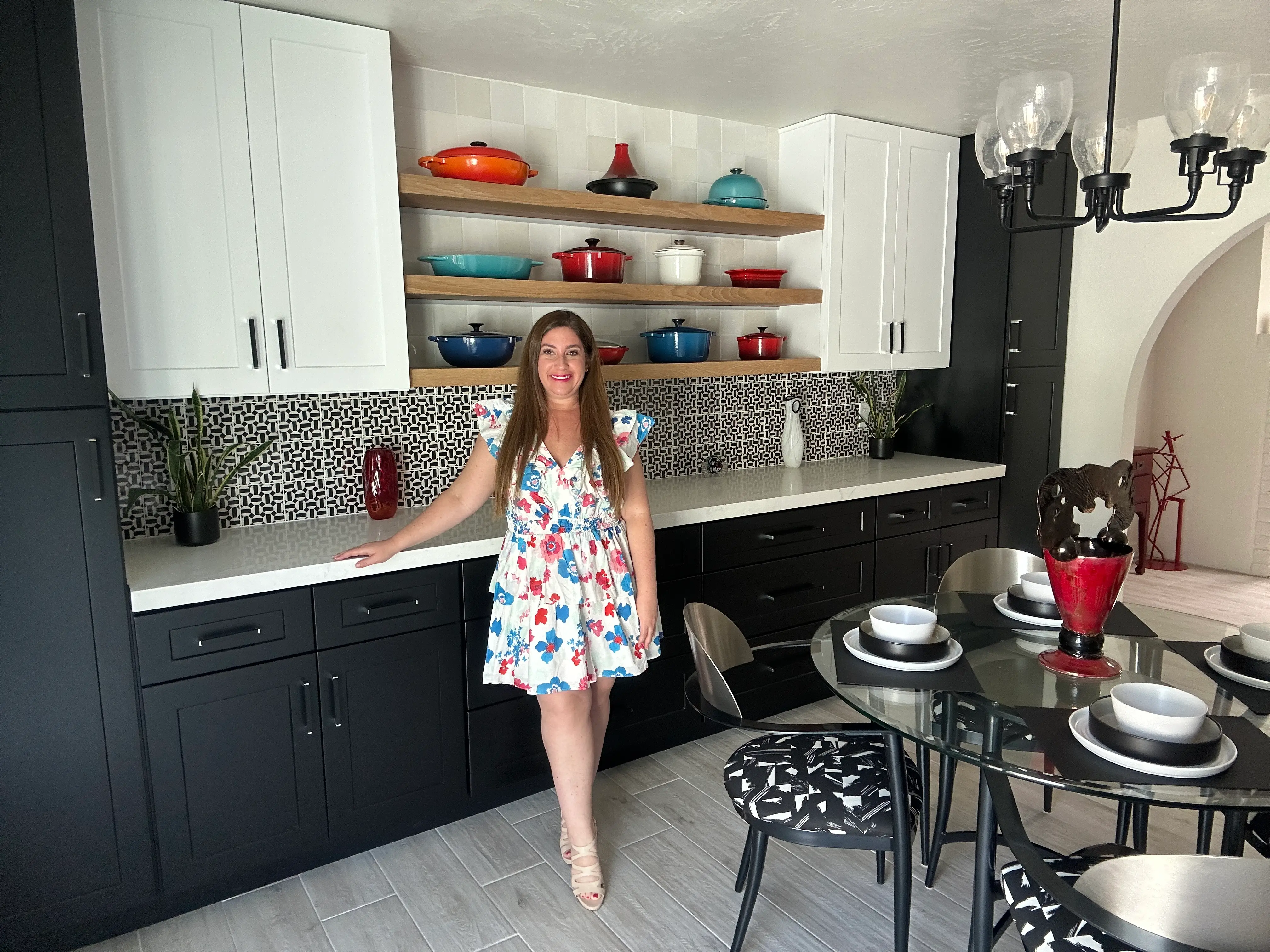 Author Jill Schildhouse smiling in her kitchen with black lower cabinets, white countertops, and white upper cabinets and a geometric. black and white backdrop