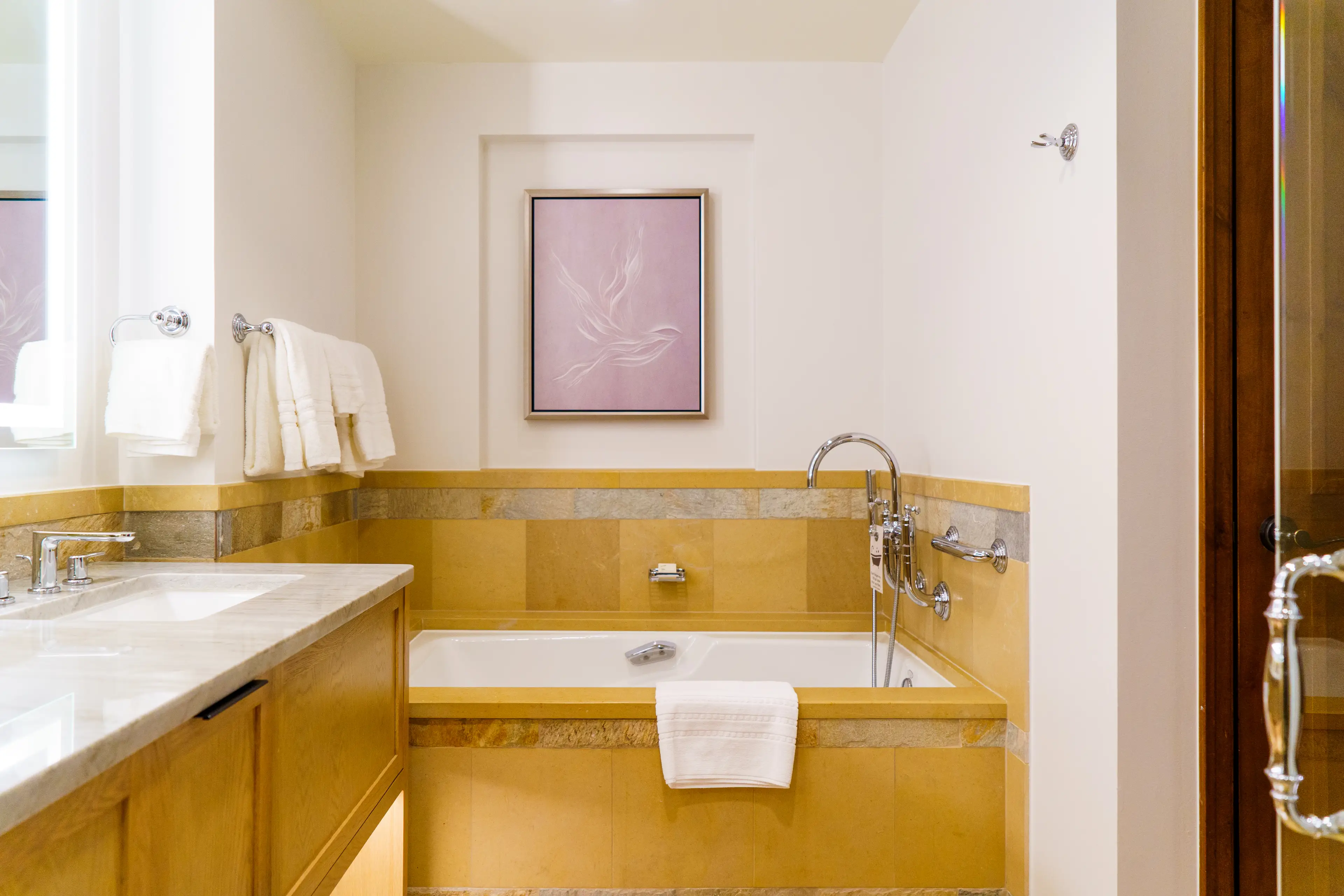 Inside a hotel bathroom with beige stone tiling, a marble sink on the left and a bathtub on the right