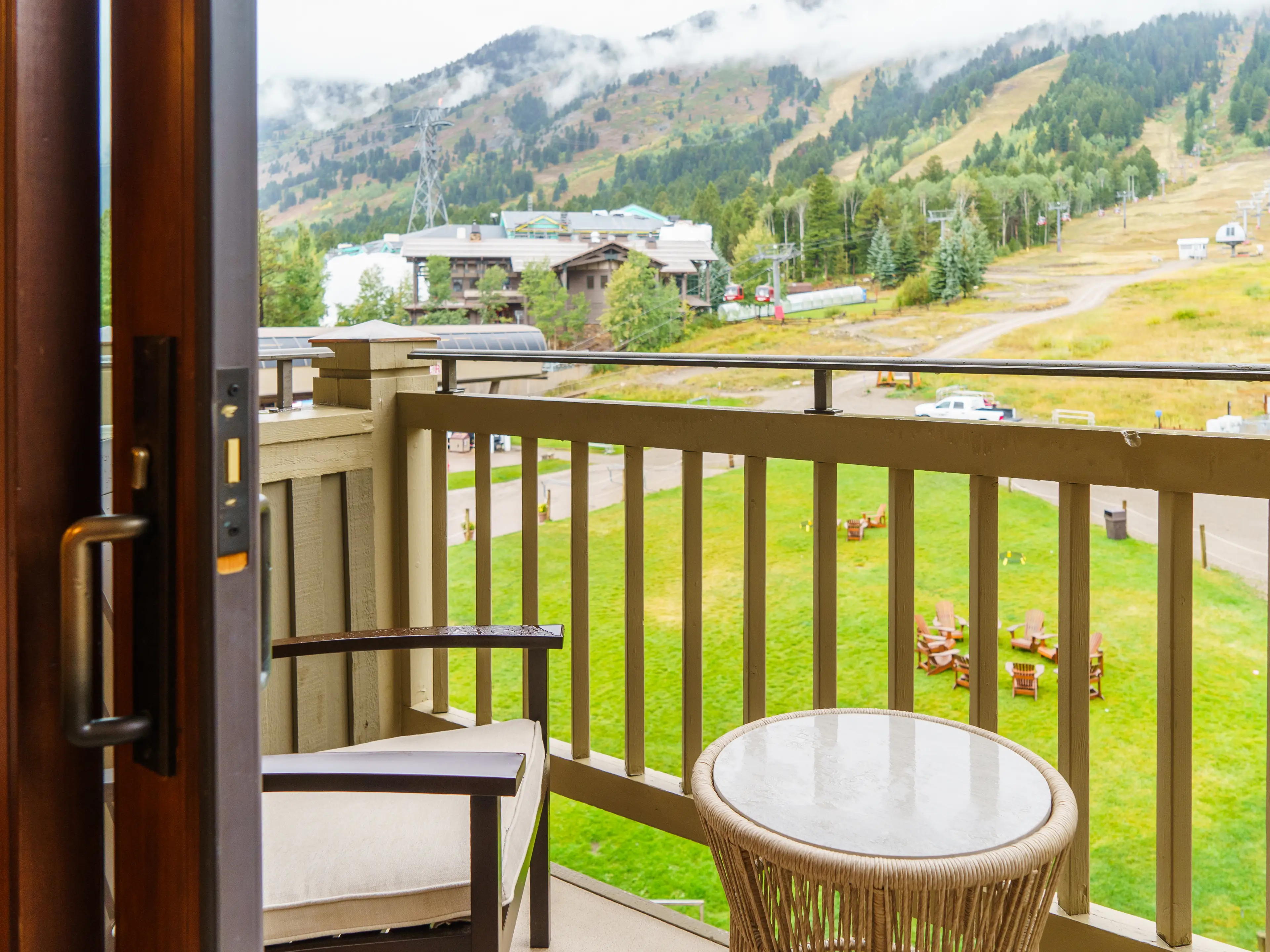 A wood sliding door opens to reveal a small hotel balcony with a mountain in the background on a gray, rainy day