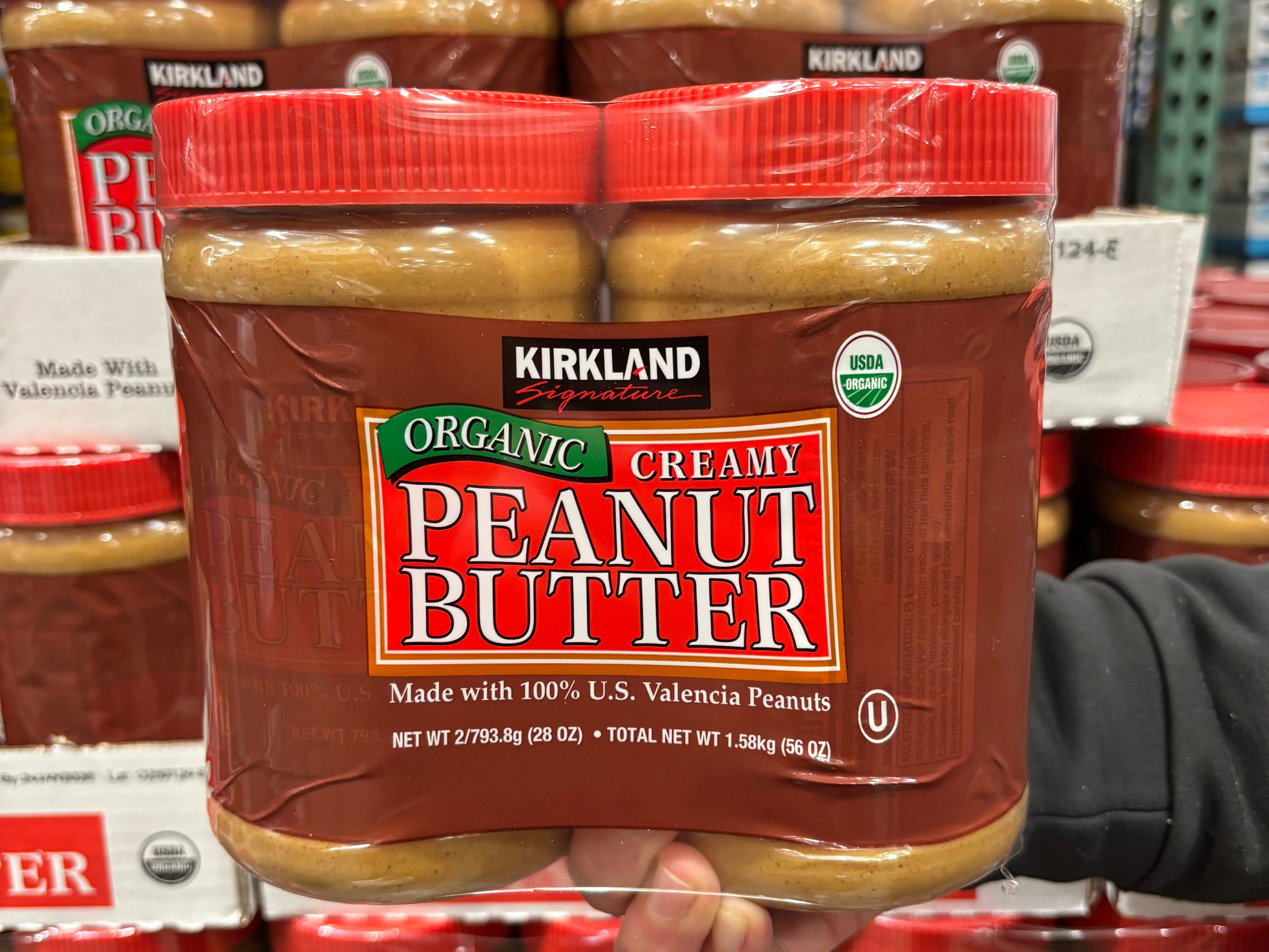A hand holding a two-pack of Kirkland Signature organic creamy peanut butter.