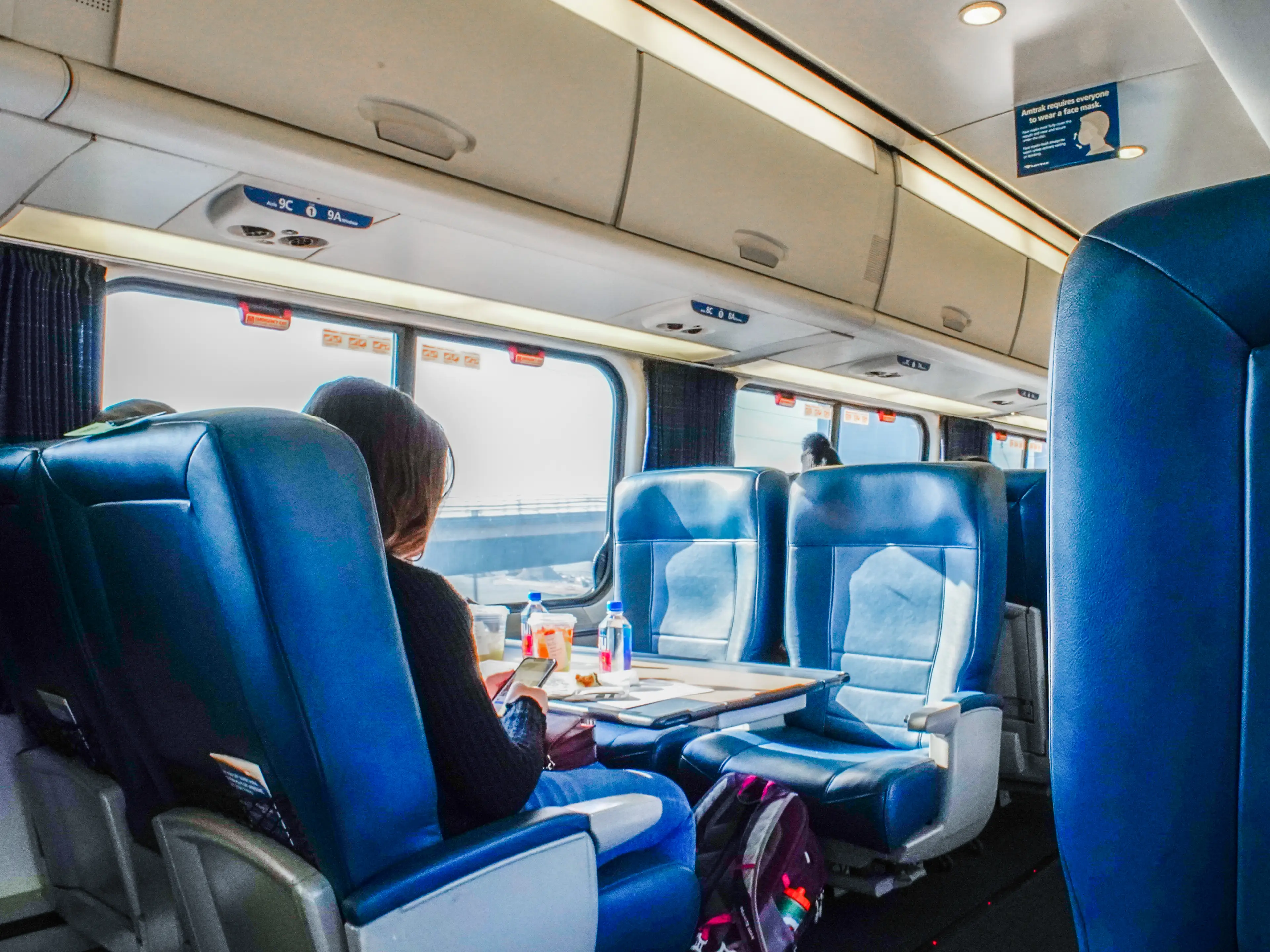 Passengers sit inside a first-class Amtrak train car with blue seats