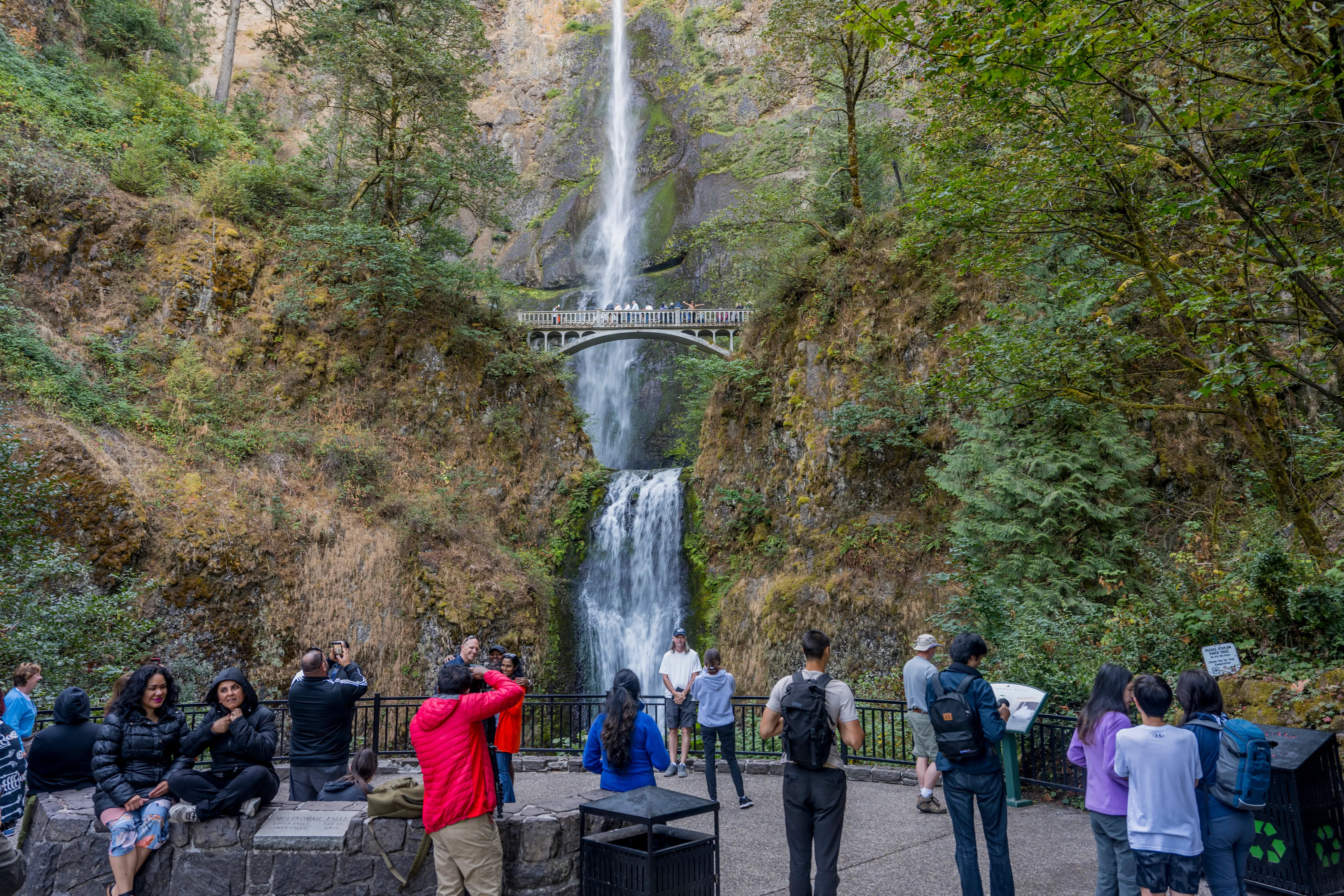 People view a waterfall that has a bridge going across it