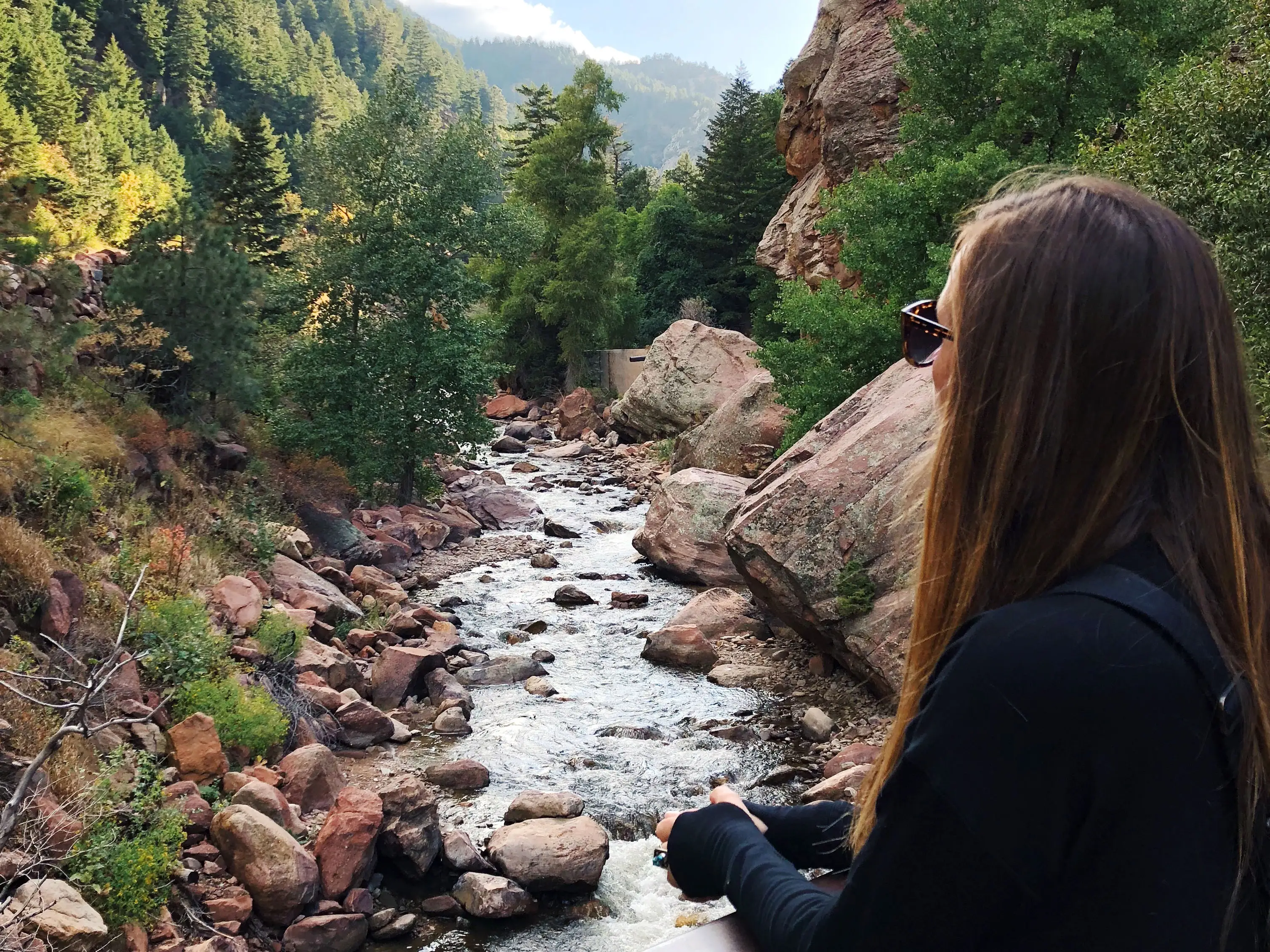 Emily stands at an overlook and looks out at a stream that runs between rocks and trees.