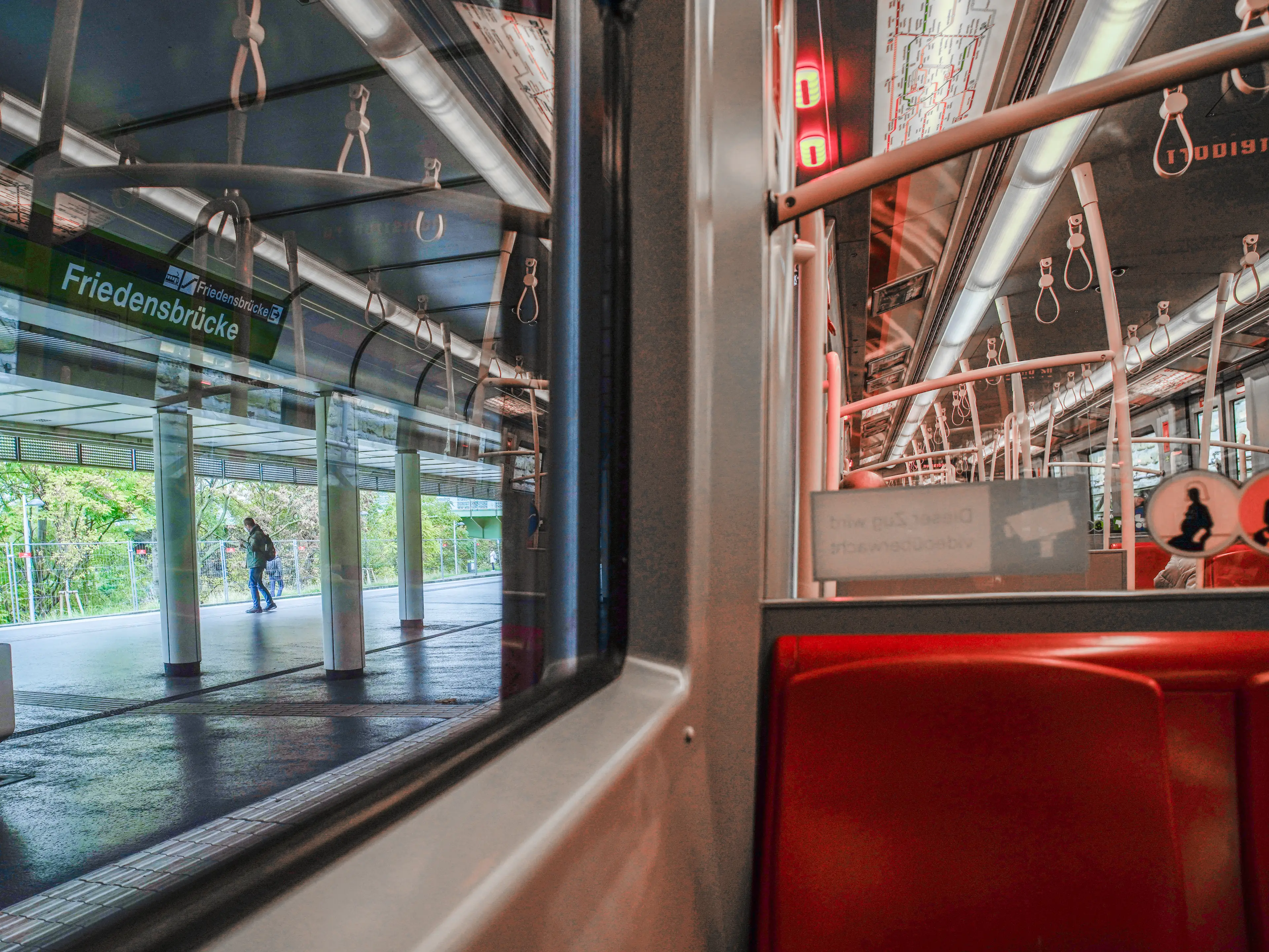 Inside a subway car with red seats and a view of the station out the window on the left in Vienna