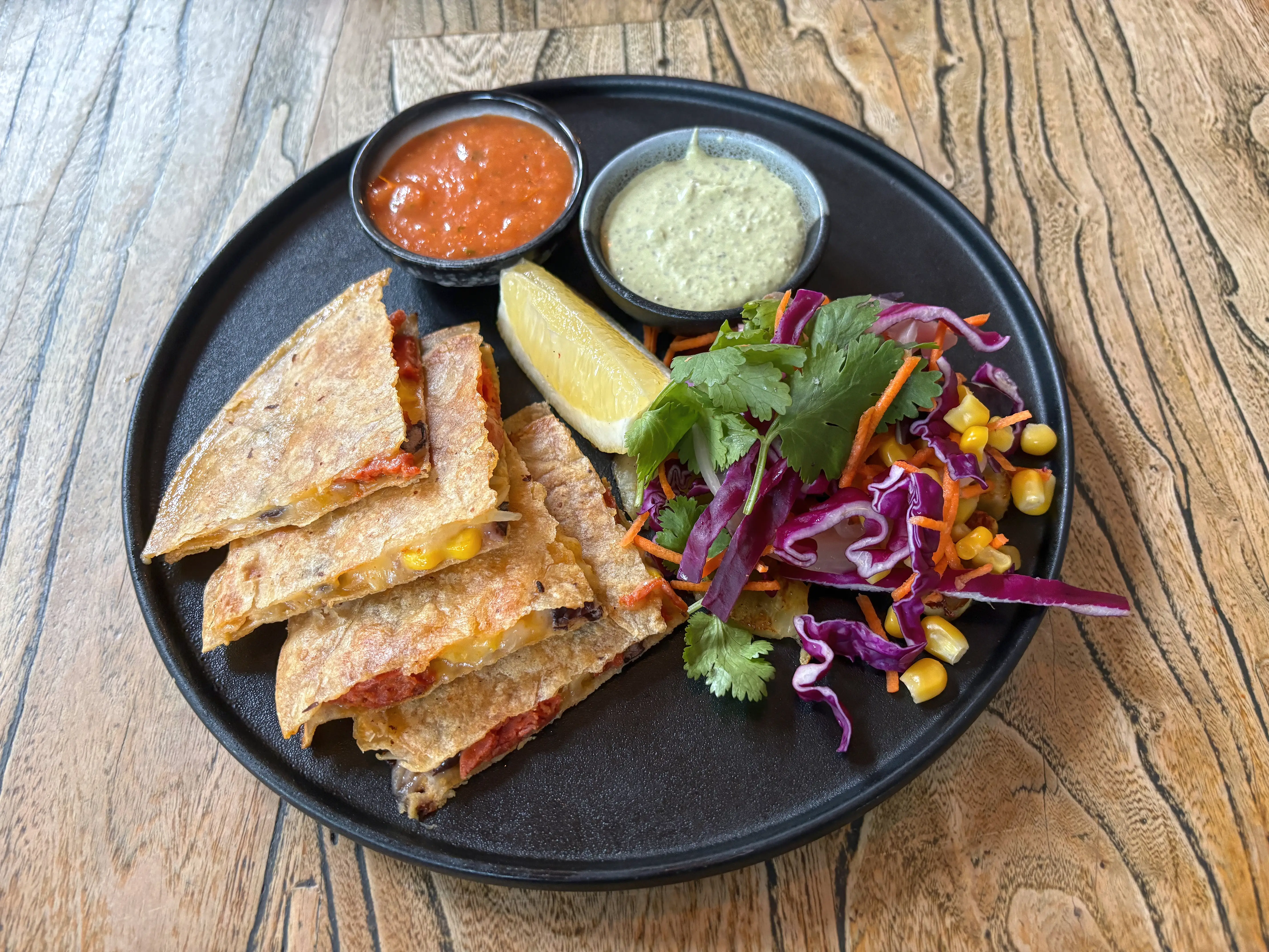 Quesadilla with vegetables, cabbage and cilantro and corn on side, and dipping sauces