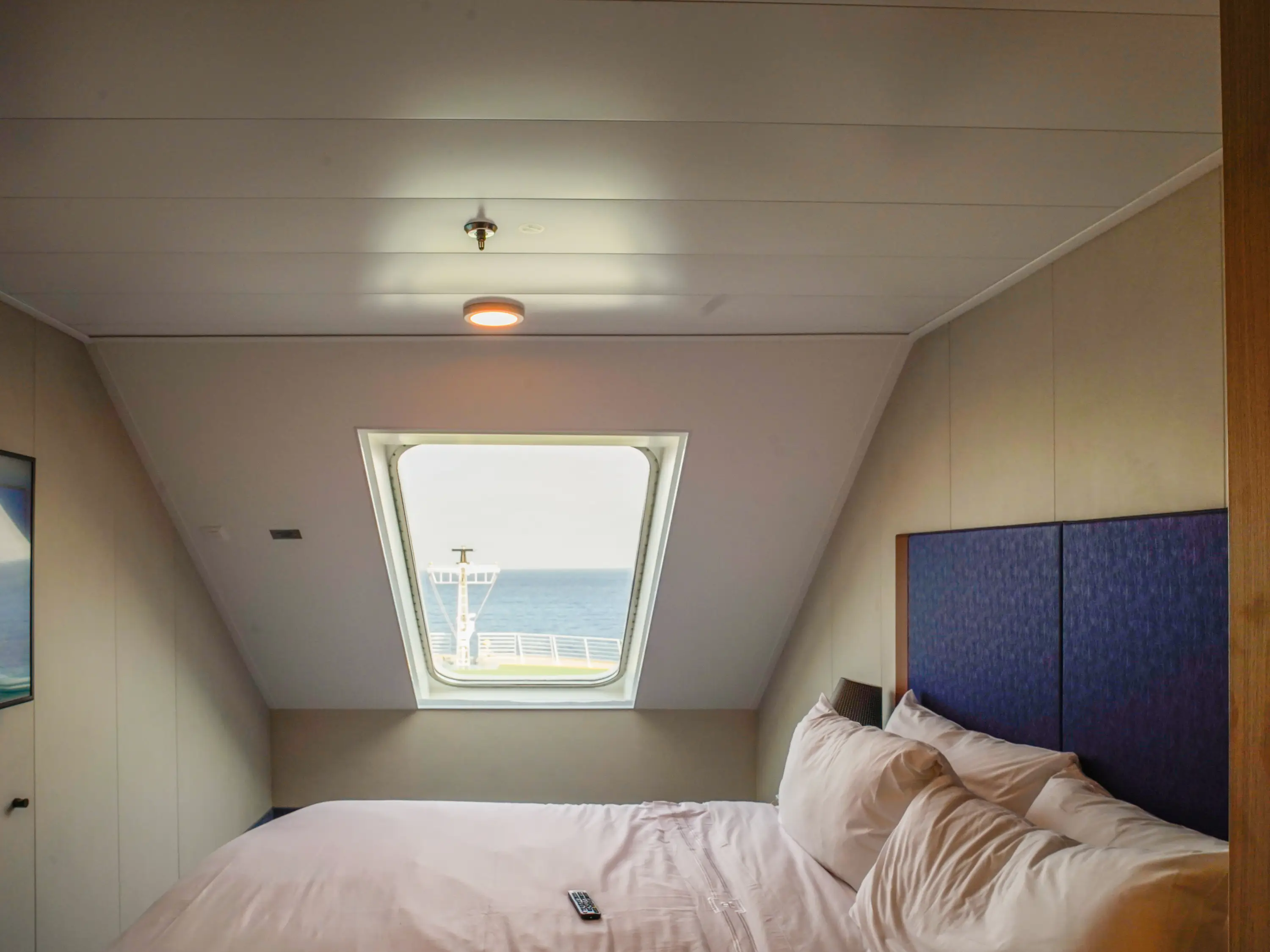 Inside a cruise ship cabin there's a bed in front of a window showing the front of the ship