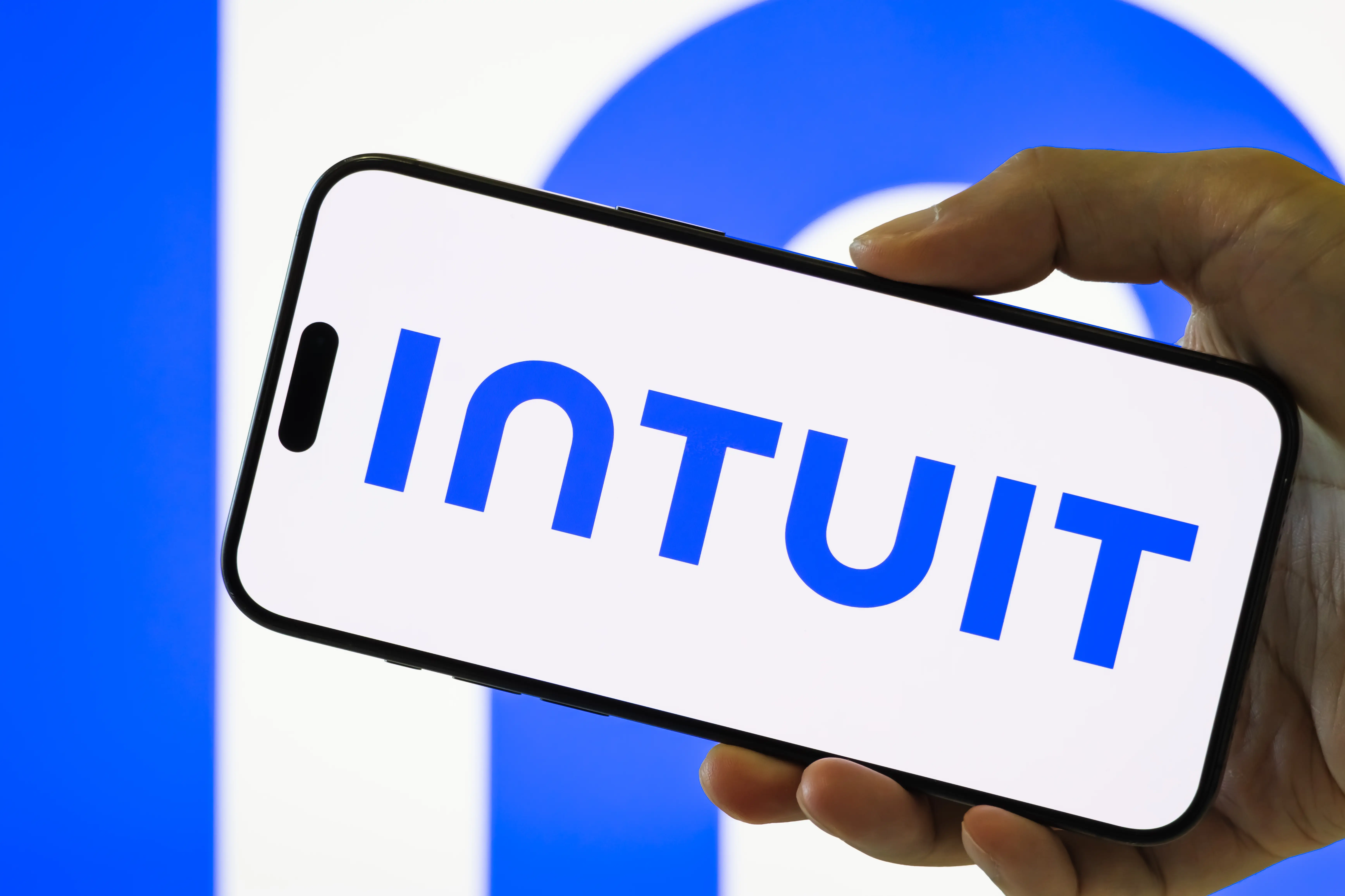 In this photo illustration, a person holds a smartphone displaying the logo of Intuit Inc.