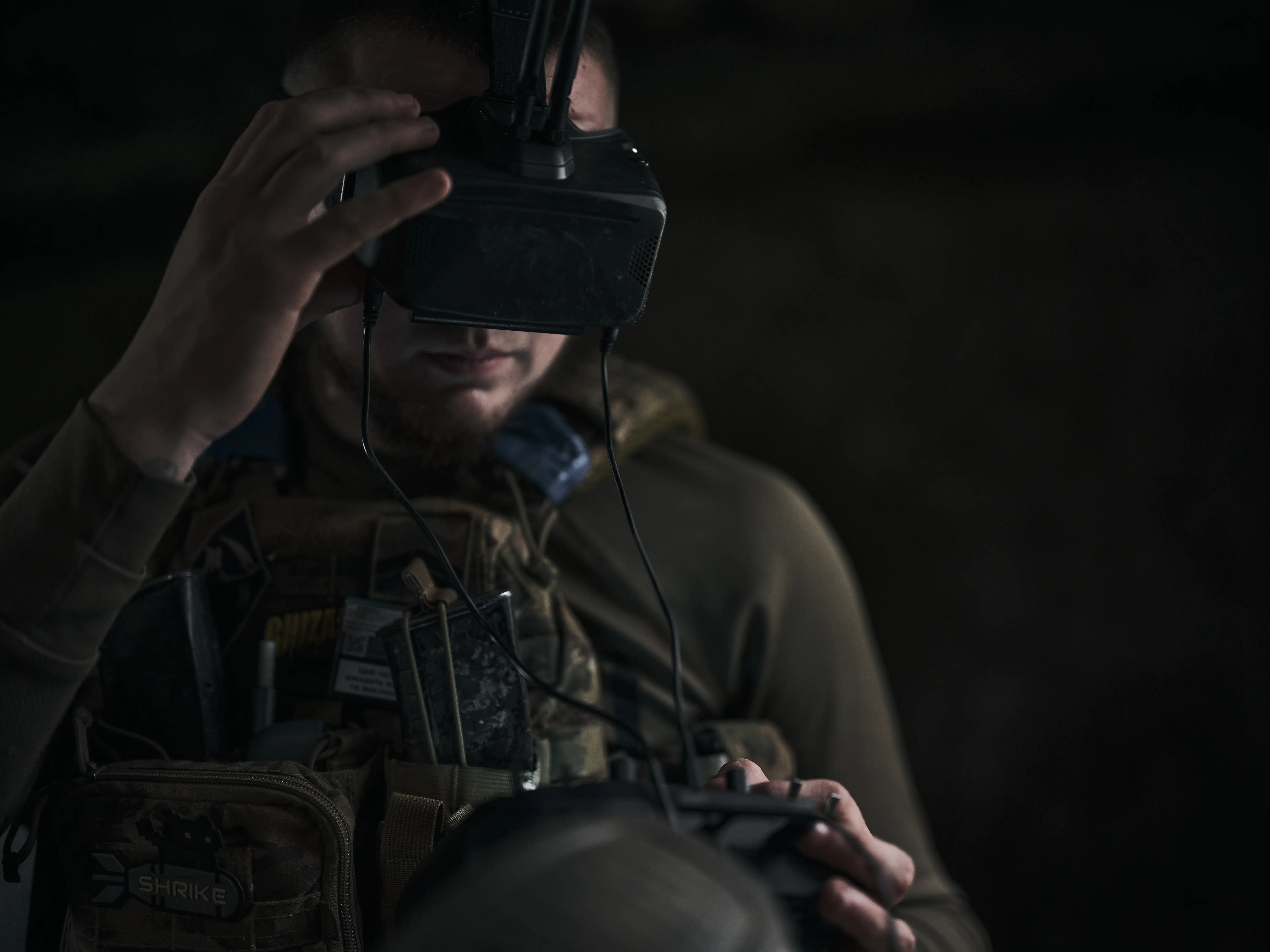 A man wearing a headset adjusts it with one hand in a dark space