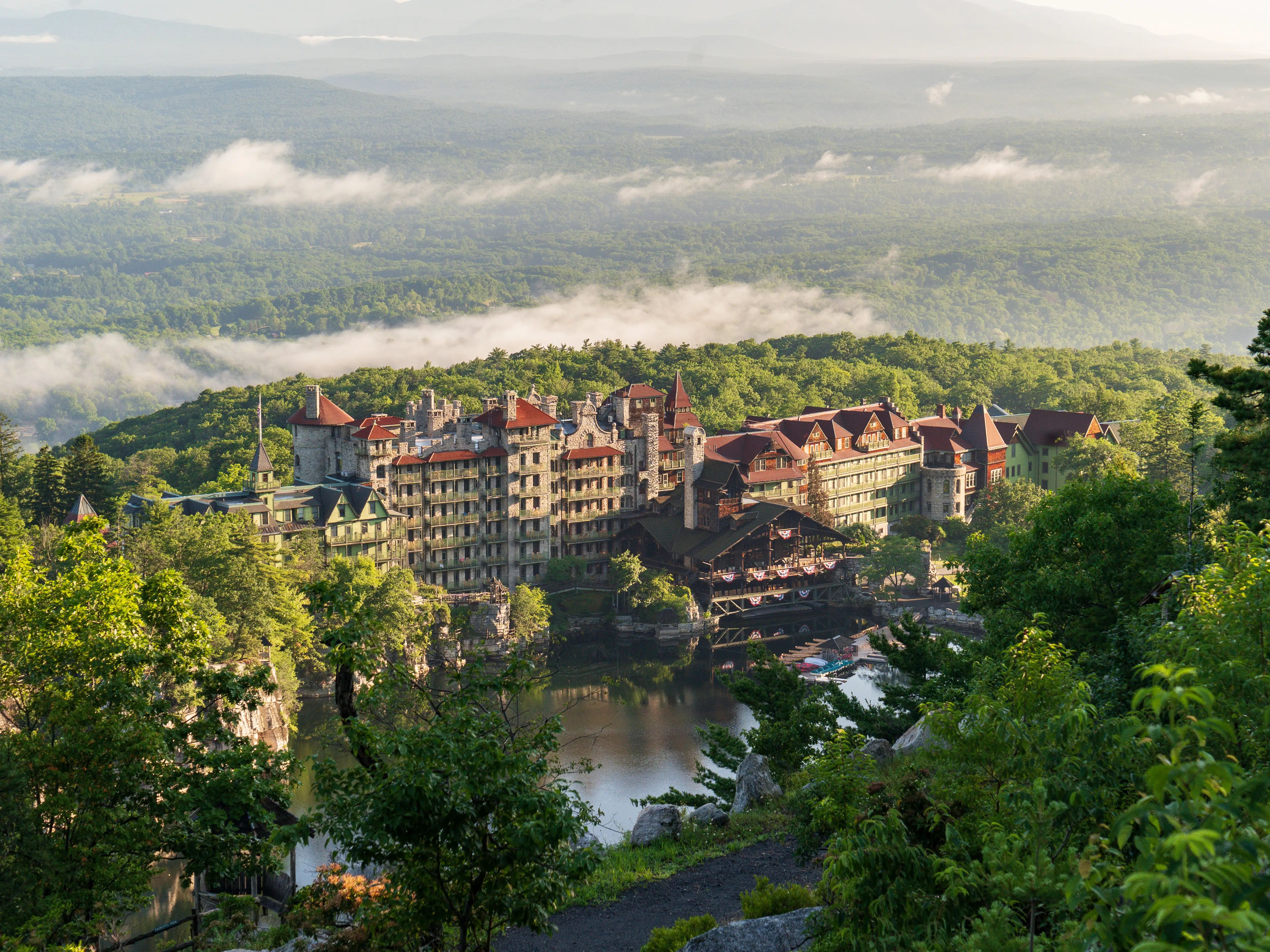 Mohonk Mountain House sits beside a lake amid forested mountains and low morning clouds.