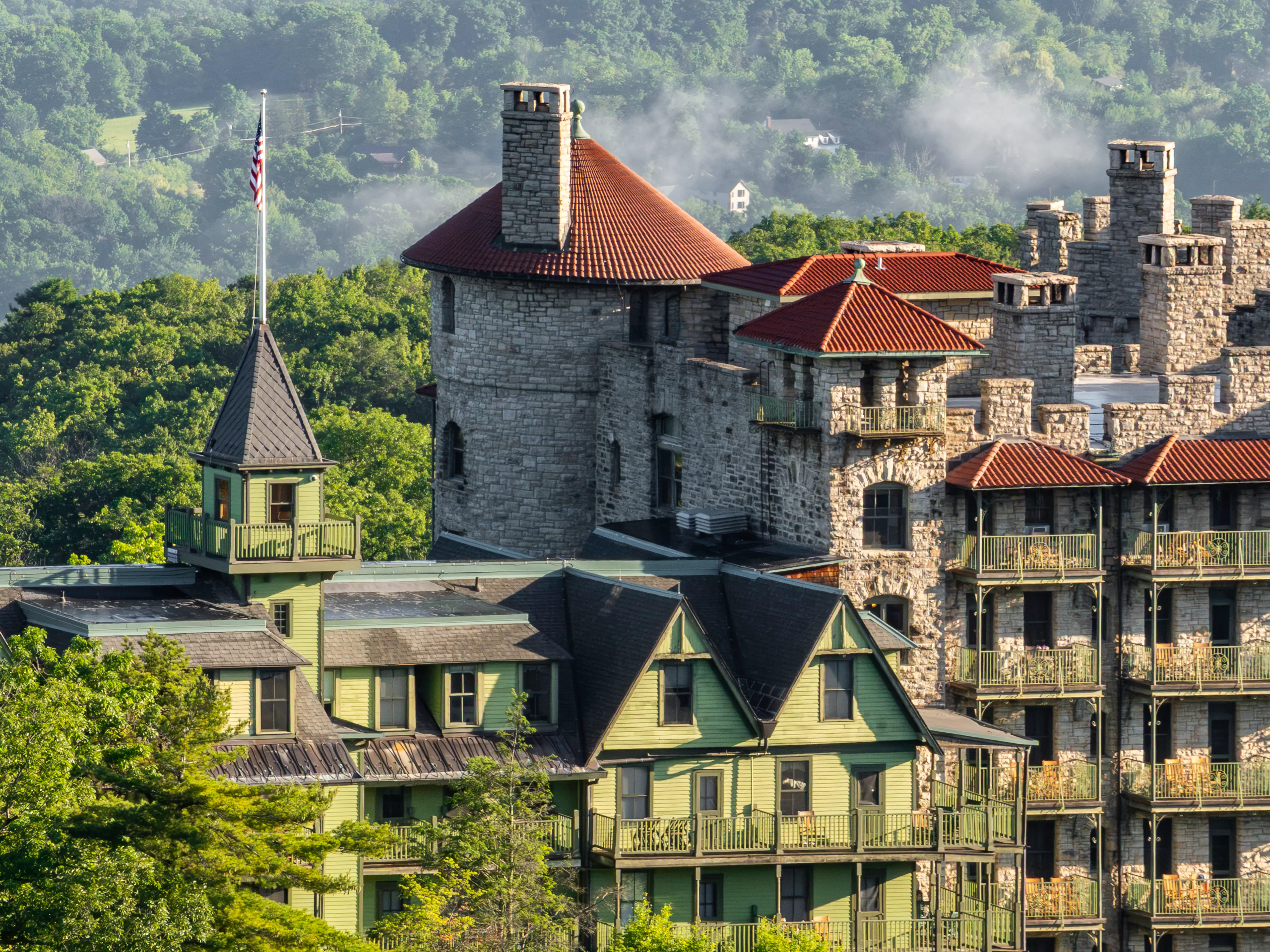 Mohonk Mountain House buildings rise above trees with stone towers, red roofs, balconies, and an American flag.