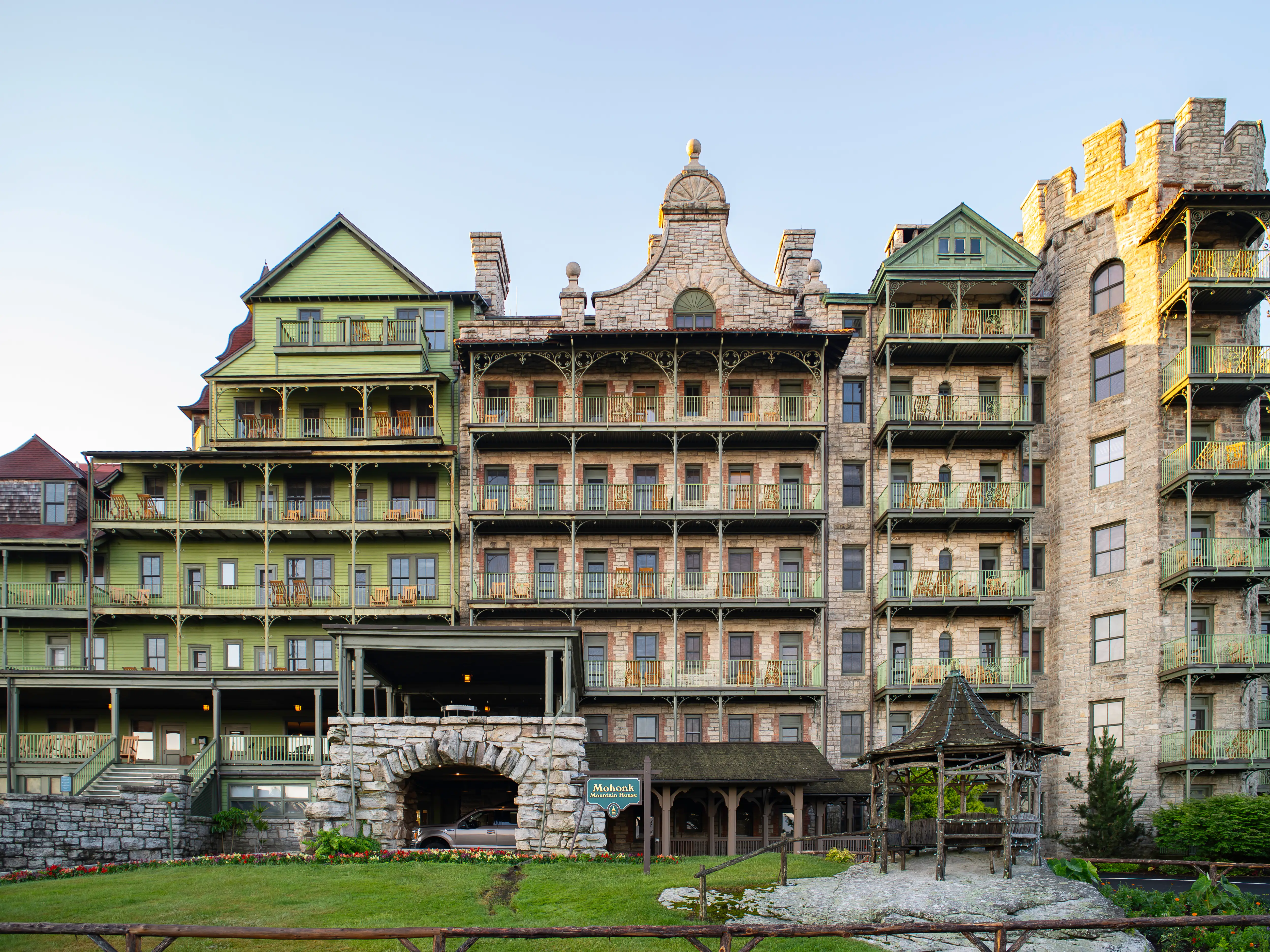 Historic Mohonk Mountain House facade with balconies, stone towers, lawn, and gazebo in clear daylight.