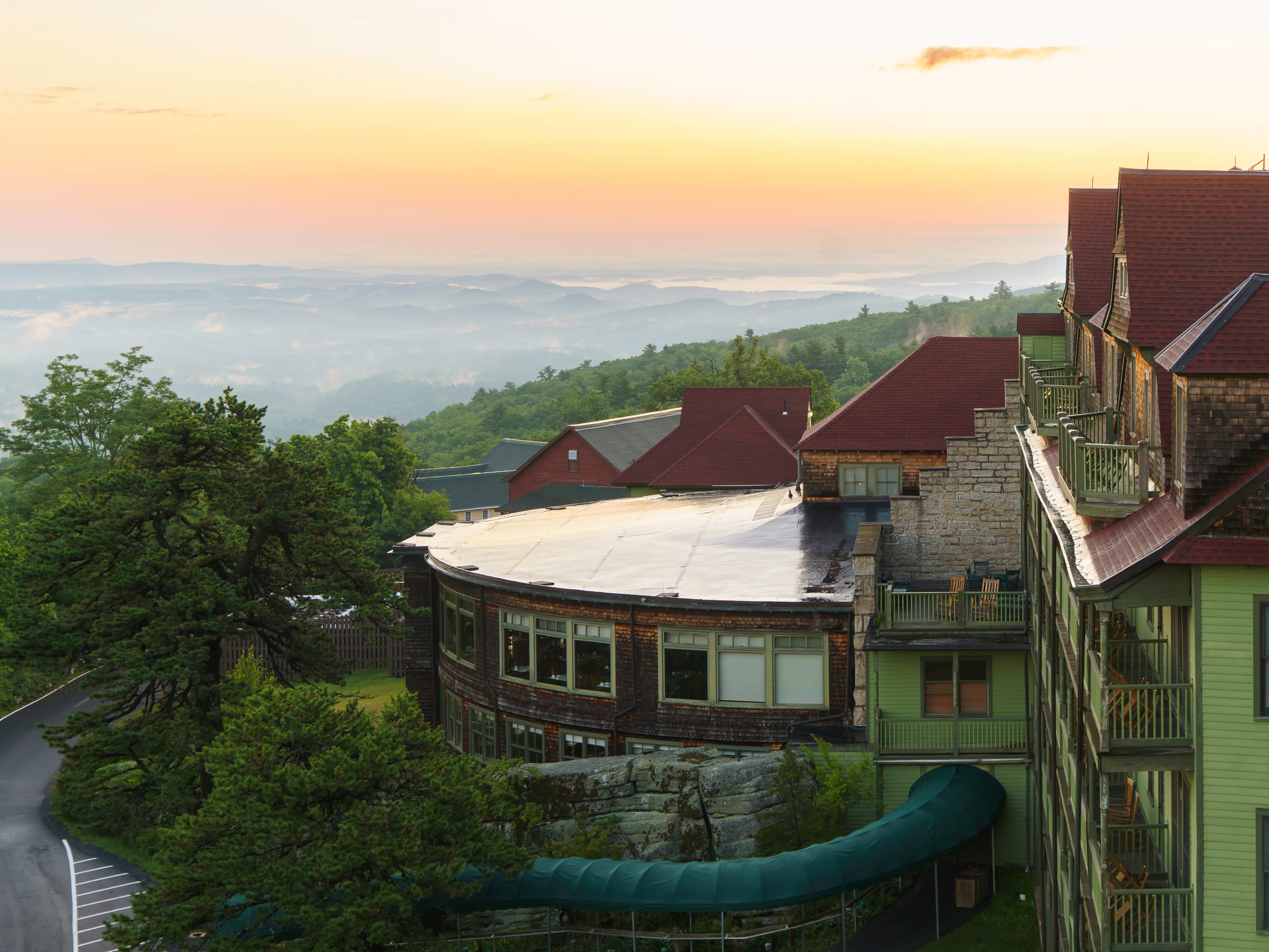 Historic mountain resort buildings overlook forested ridges under a pastel sunrise sky.