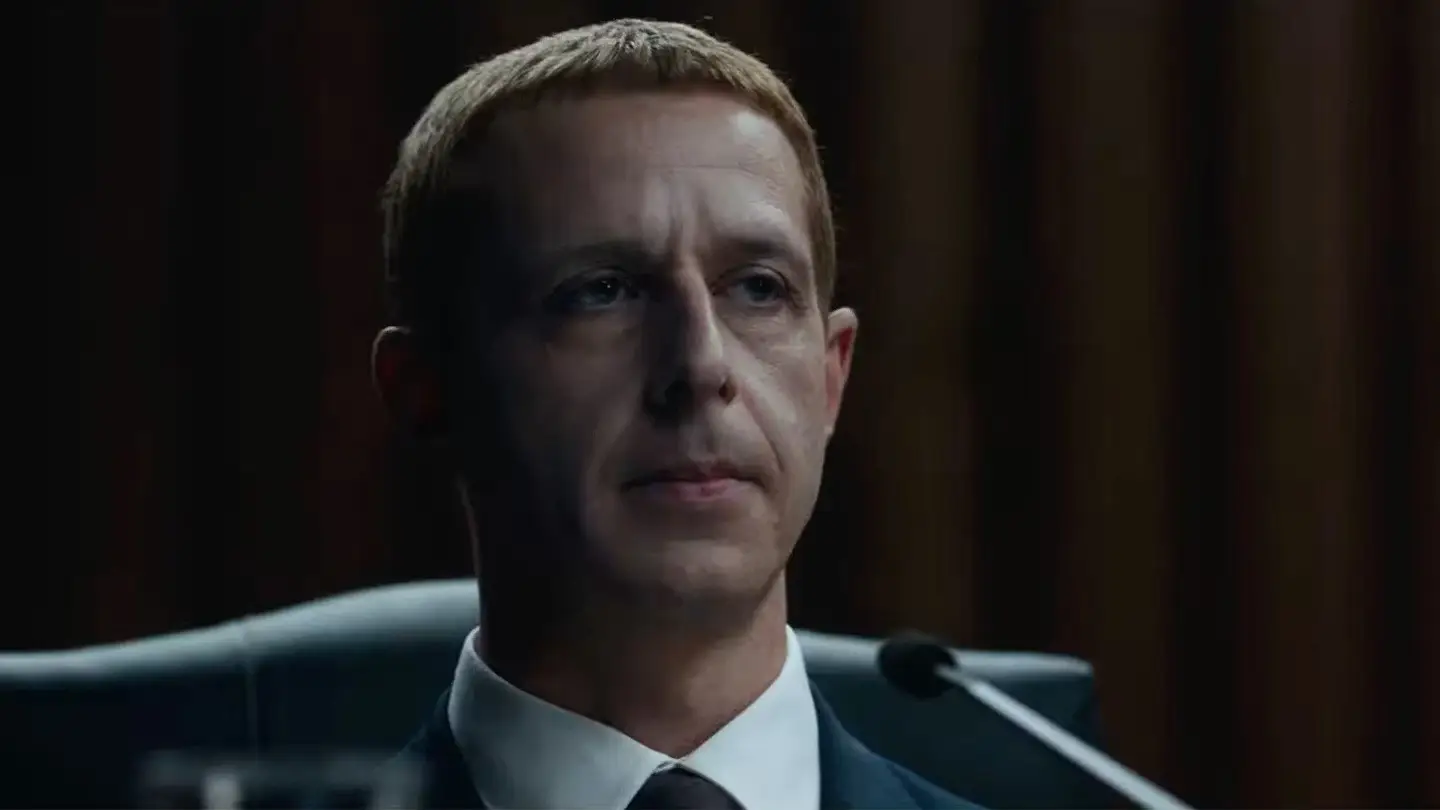 Jeremy Strong sitting in a chair with a microphone in front of him as Mark Zuckerberg