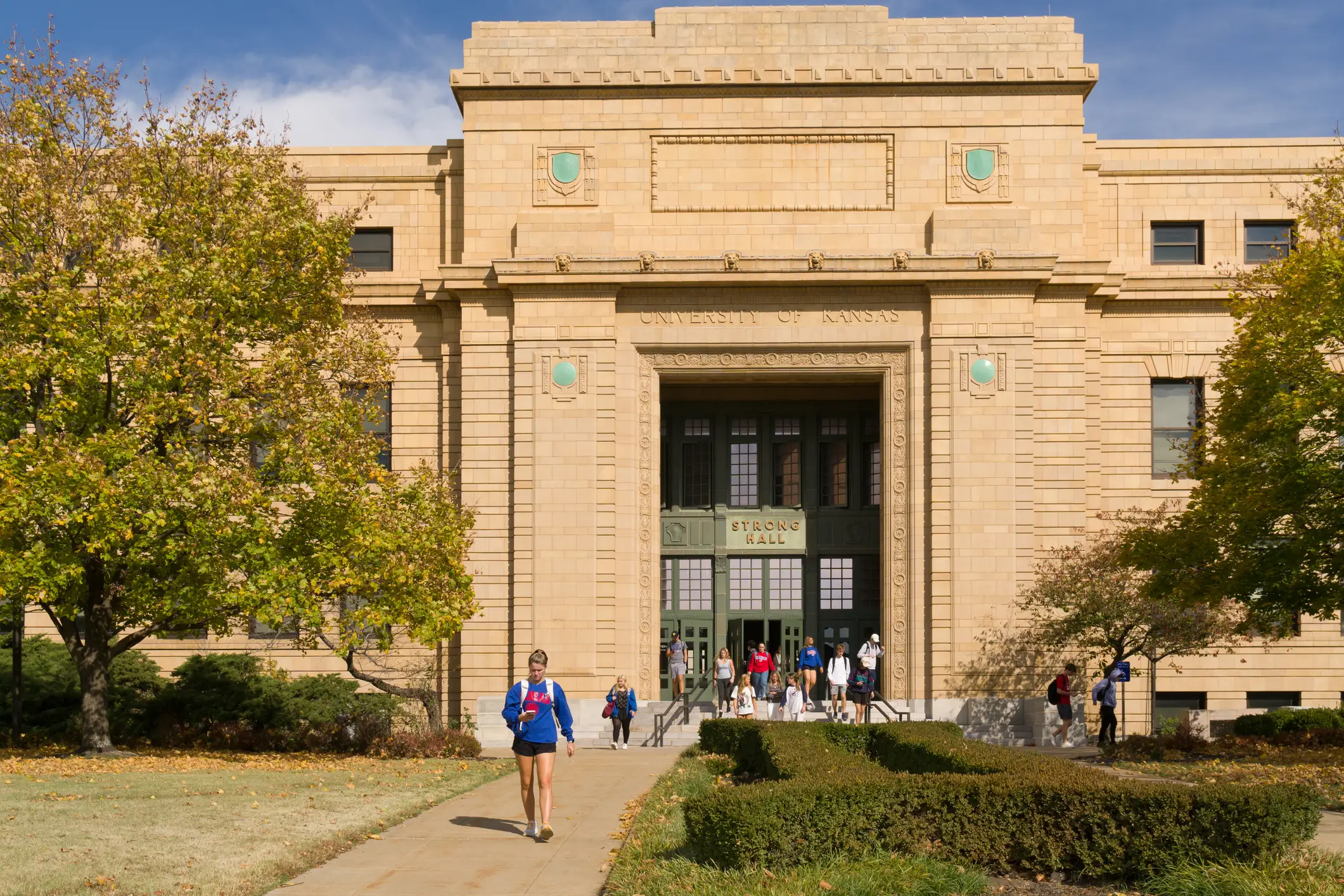 Students walk outside the University of Kansas Budig Hall and Hoch Auditorium entrance on a sunny campus day.
