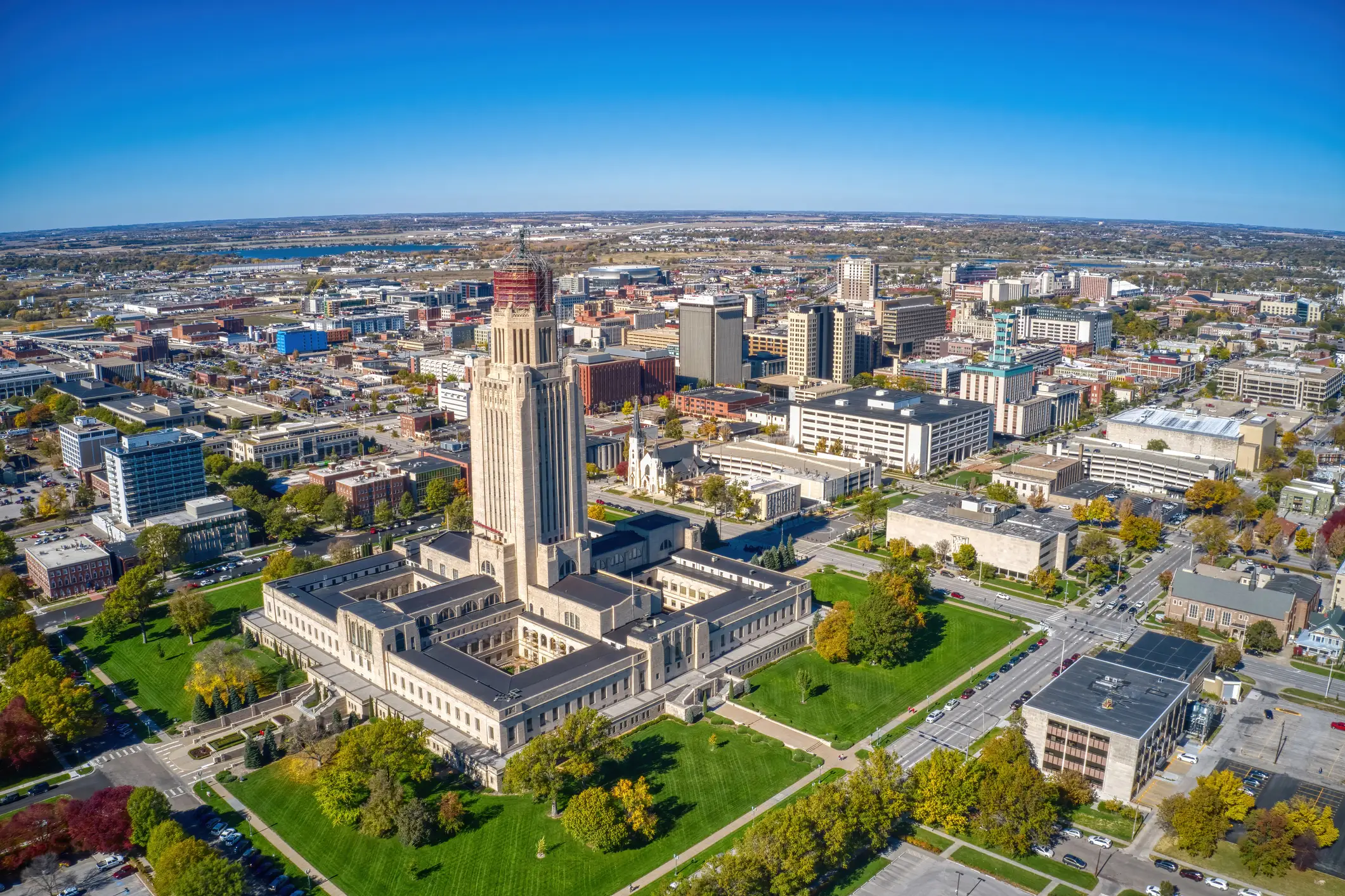 Aerial view of the Nebraska State Capitol surrounded by downtown Lincoln streets, buildings, lawns, and autumn trees.