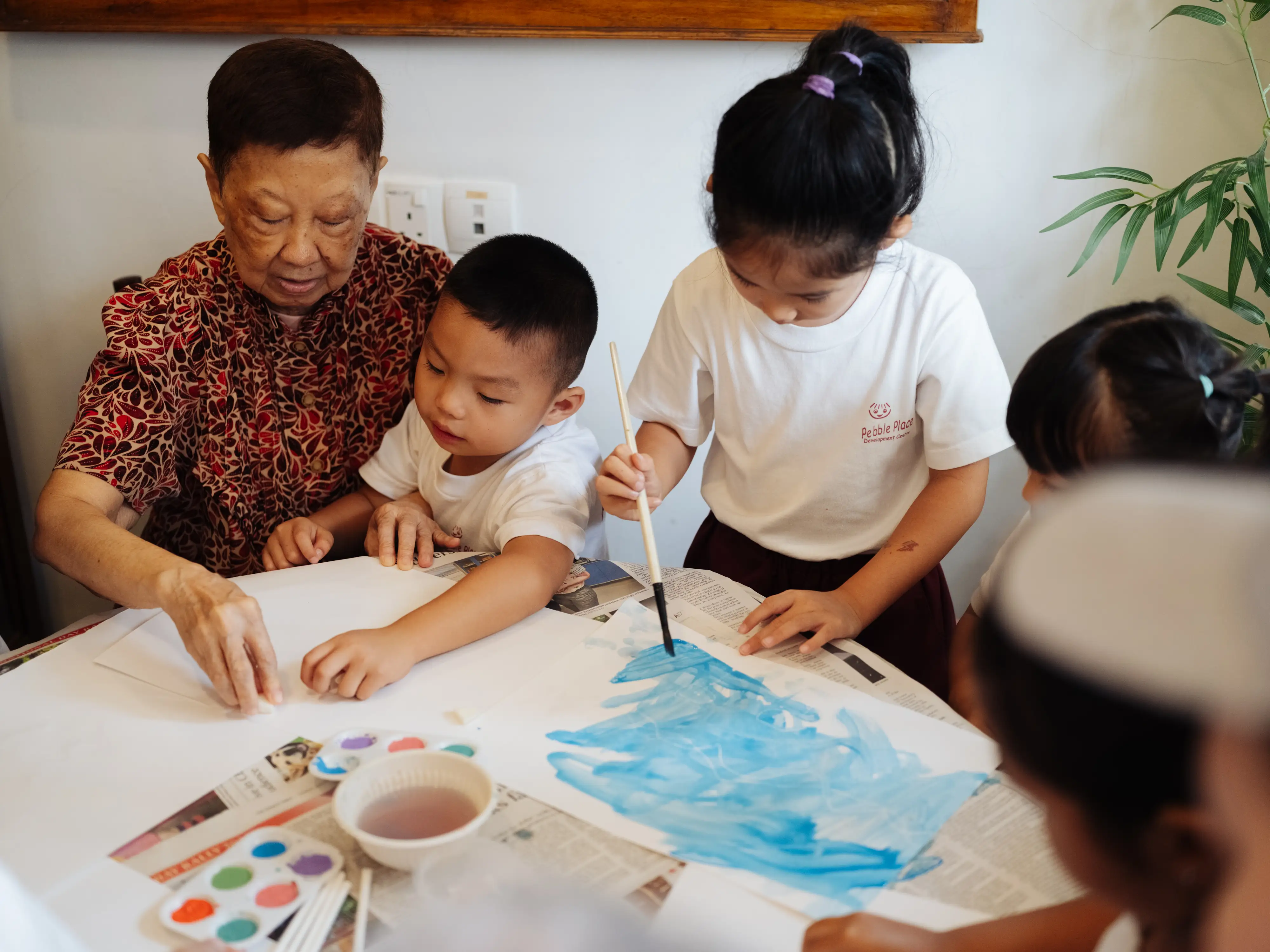 Kids and an older lady painting together.