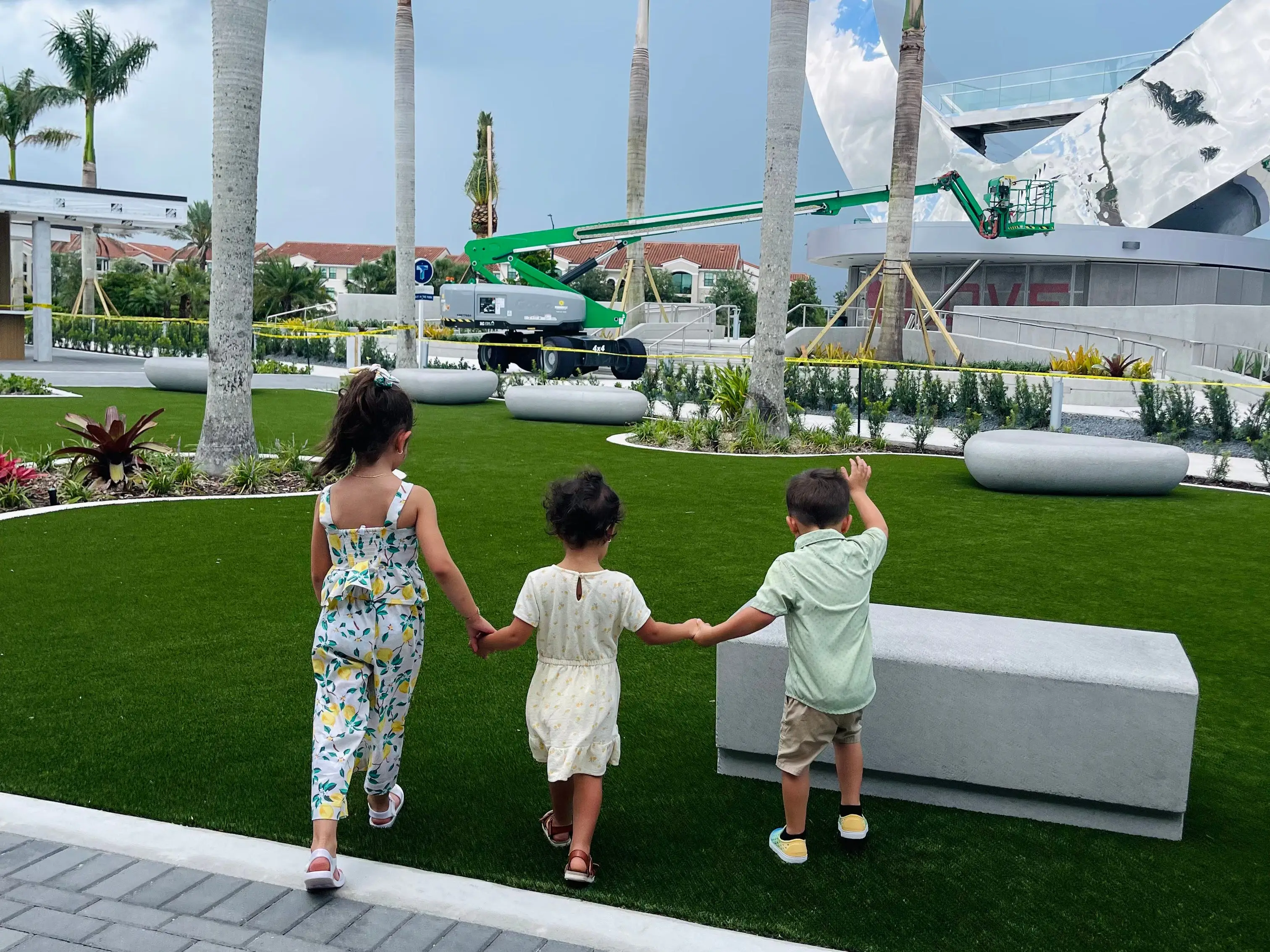 kids holding hands near palm trees on patch of turf
