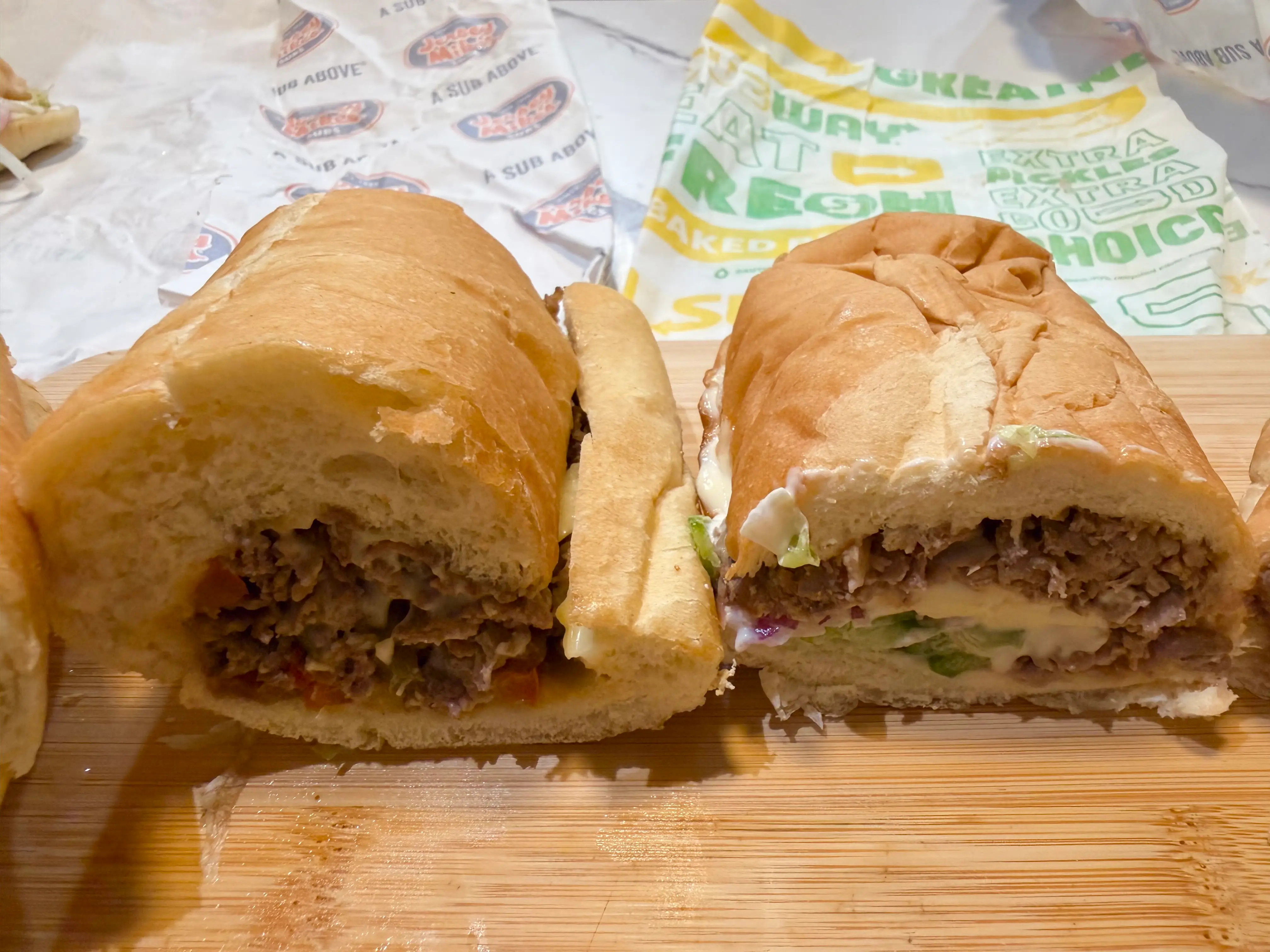 Half of Jersey Mikes philly cheesesteak next to half of subway cheesesteak