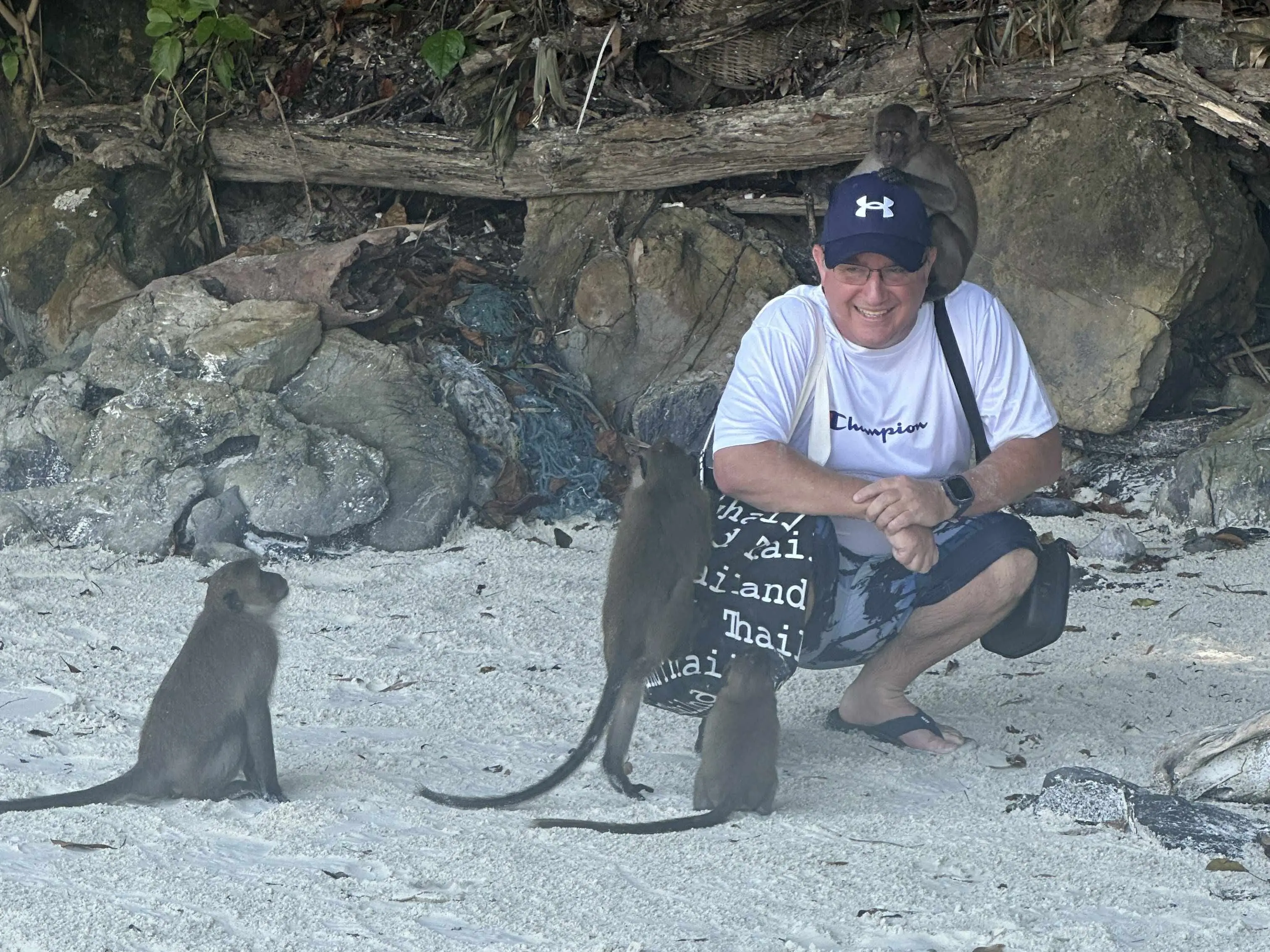A man posing with some monkeys on a beach.