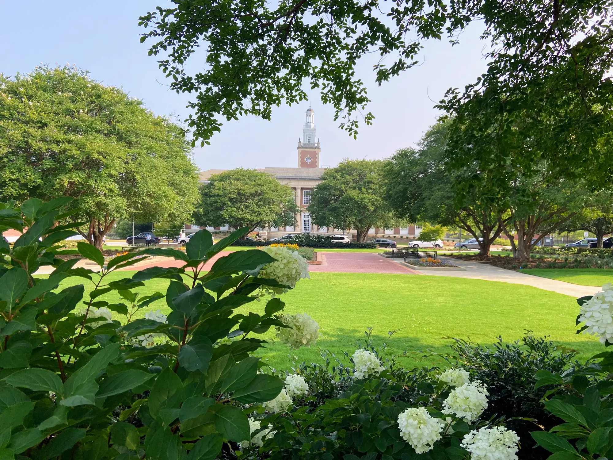 Landscaped campus lawn with white flowers and trees framing a brick building with a clock tower.