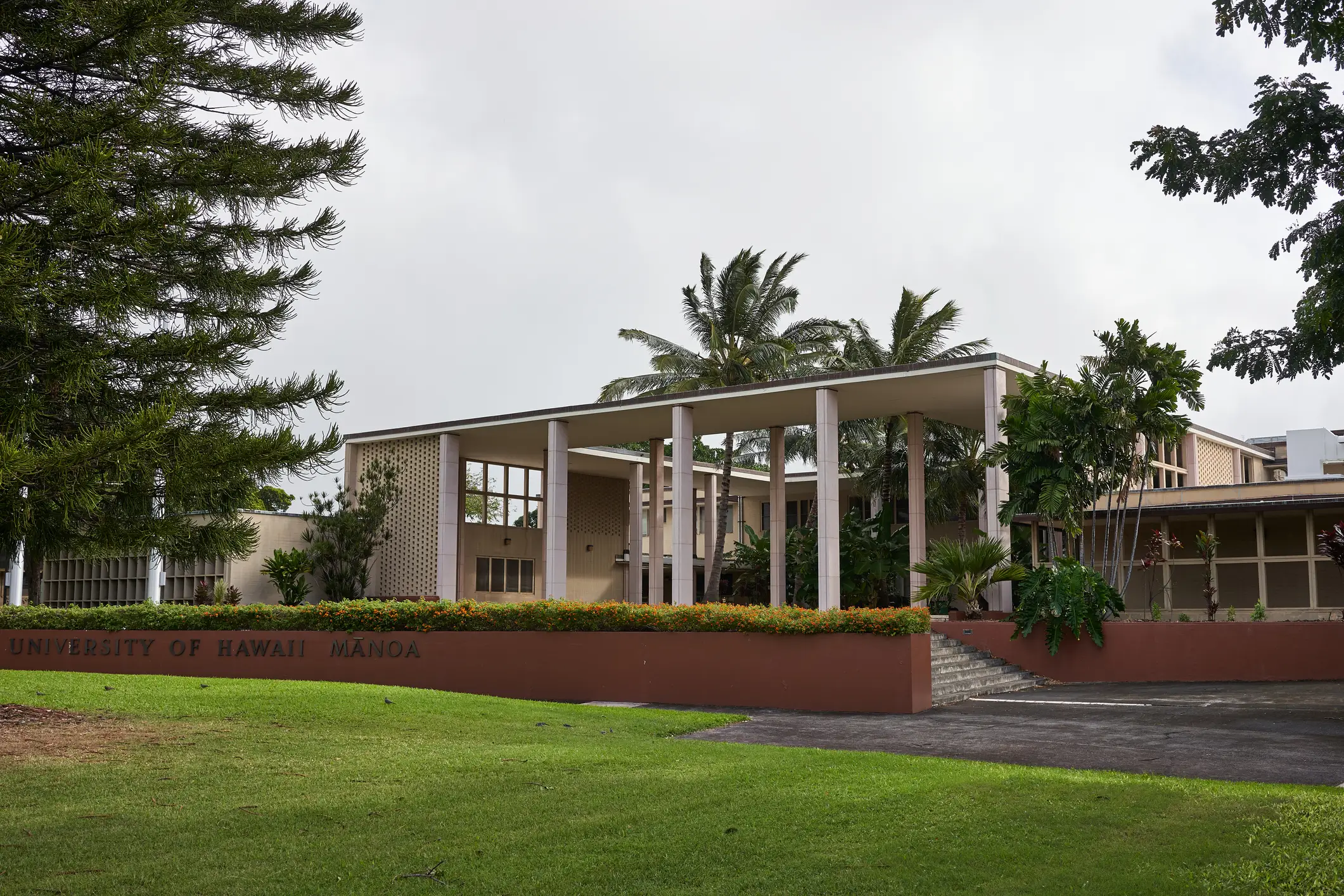 University of Hawaii Manoa campus building with columns, lawns, trees, and an overcast sky.