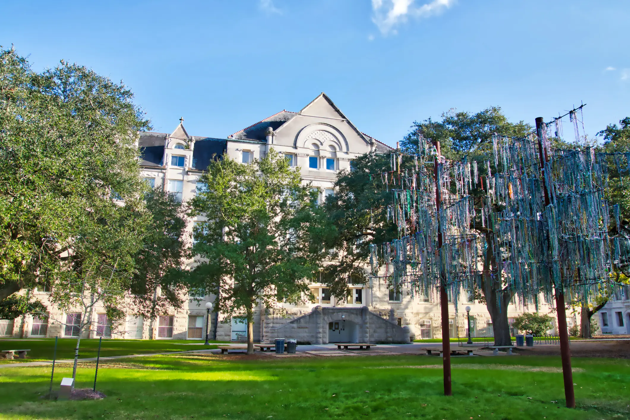 Historic stone building and shaded lawn with a tall hanging ribbon installation under a clear blue sky.