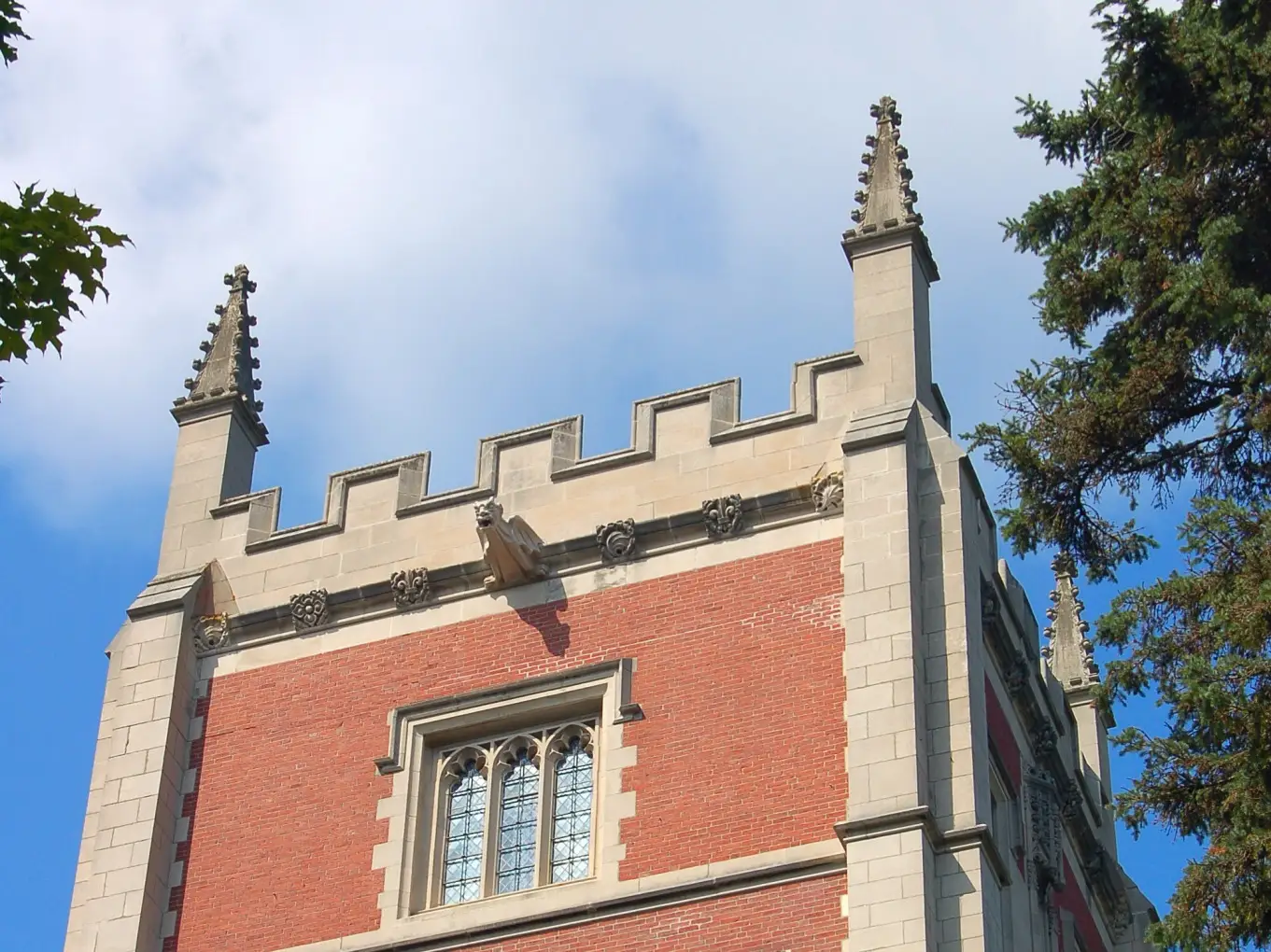 Red brick and stone Gothic-style building facade with crenellations and pointed spires against a blue sky.