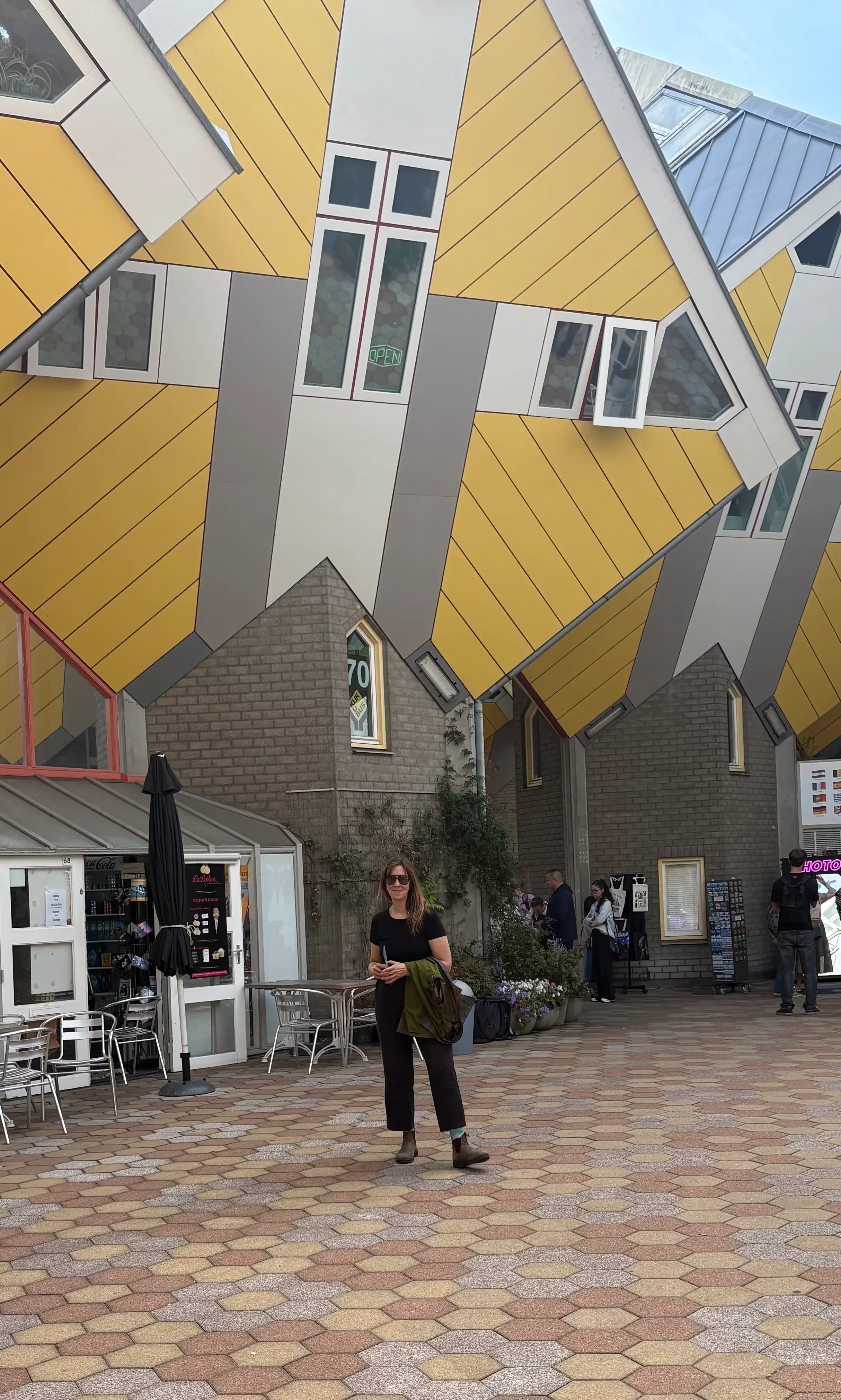 Yellow Cube Houses tower over a paved courtyard with café seating and visitors below.