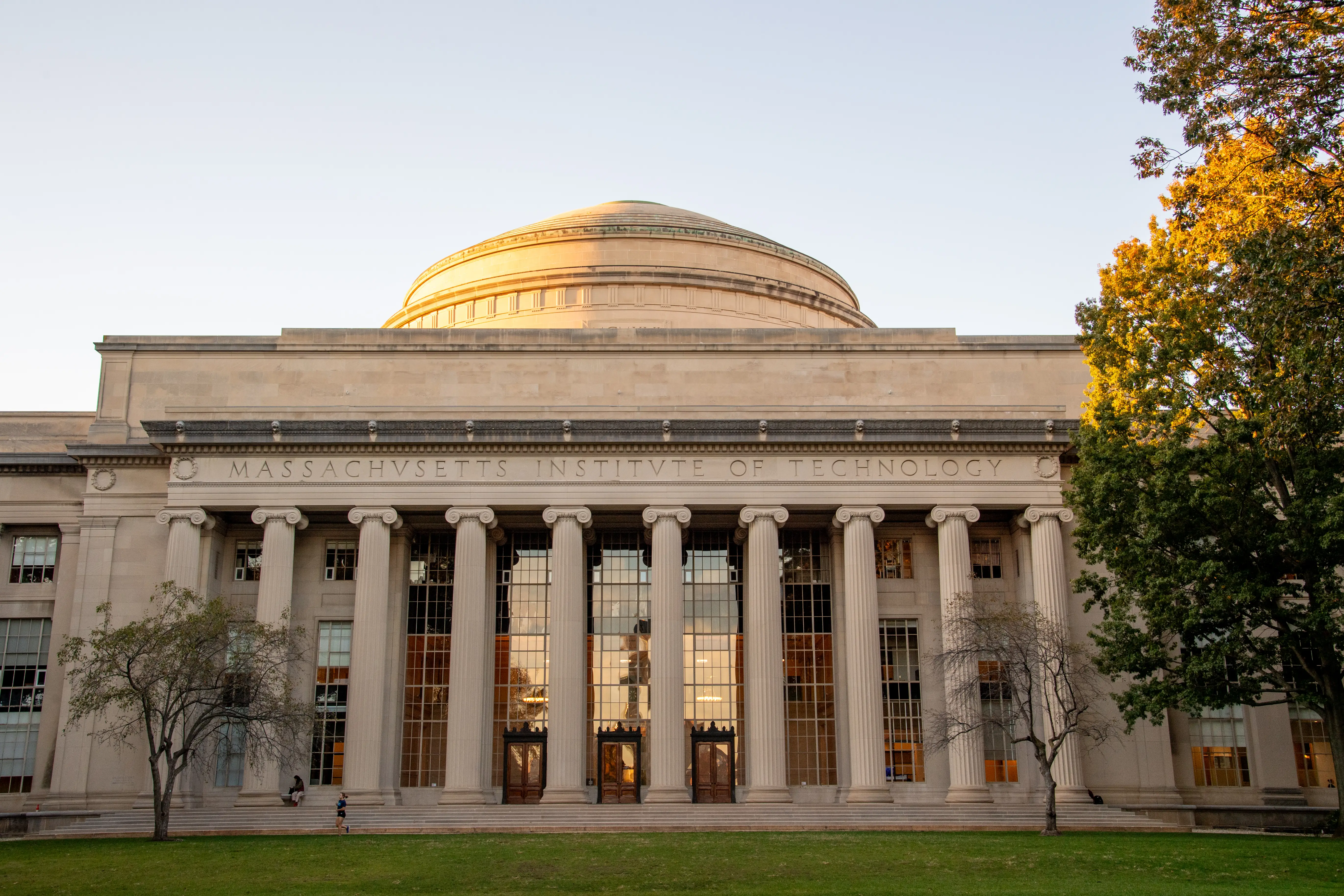 Massachusetts Institute of Technology's columned Great Dome building stands behind a lawn and autumn trees.