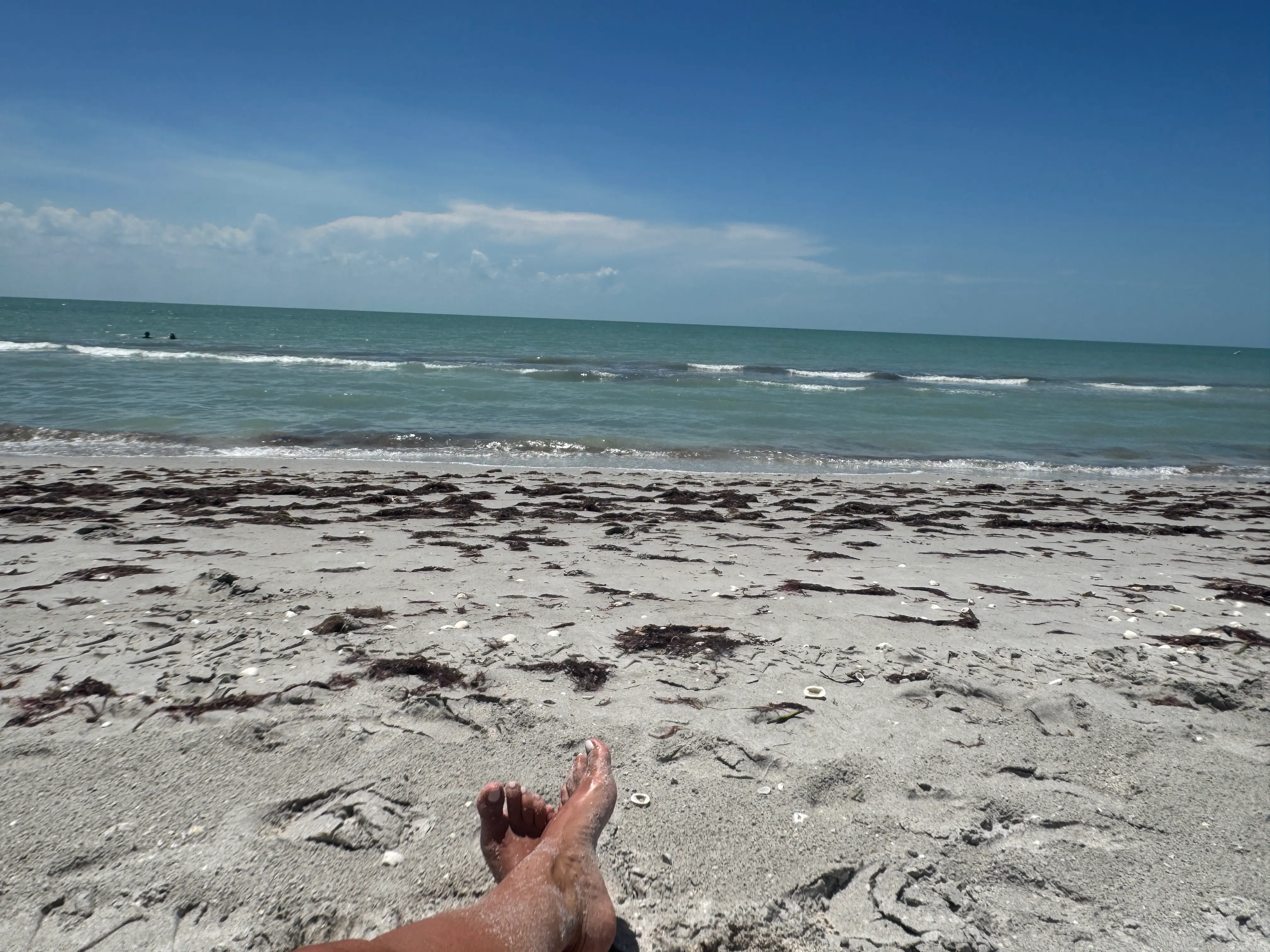 View of feet on sandy beach in front of ocean