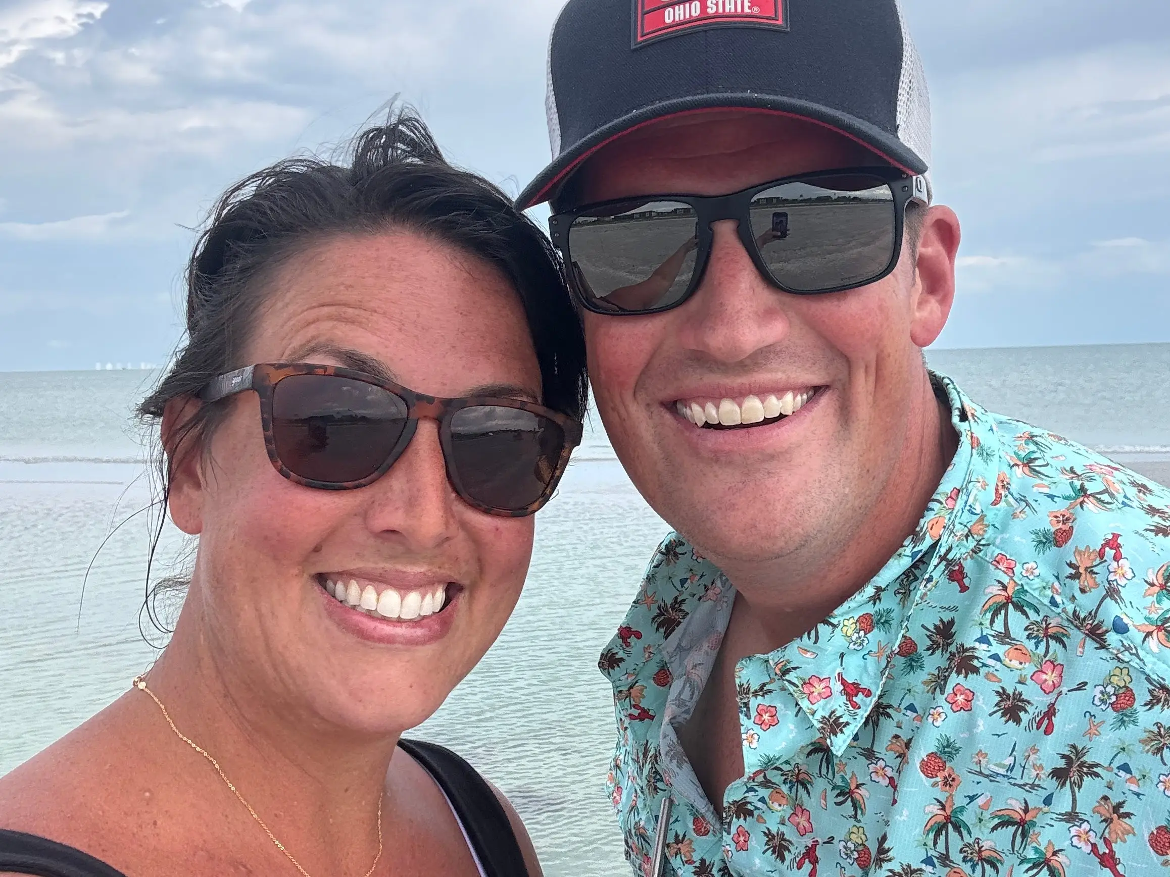 Man and woman smiling wearing sunglasses in selfie on beach