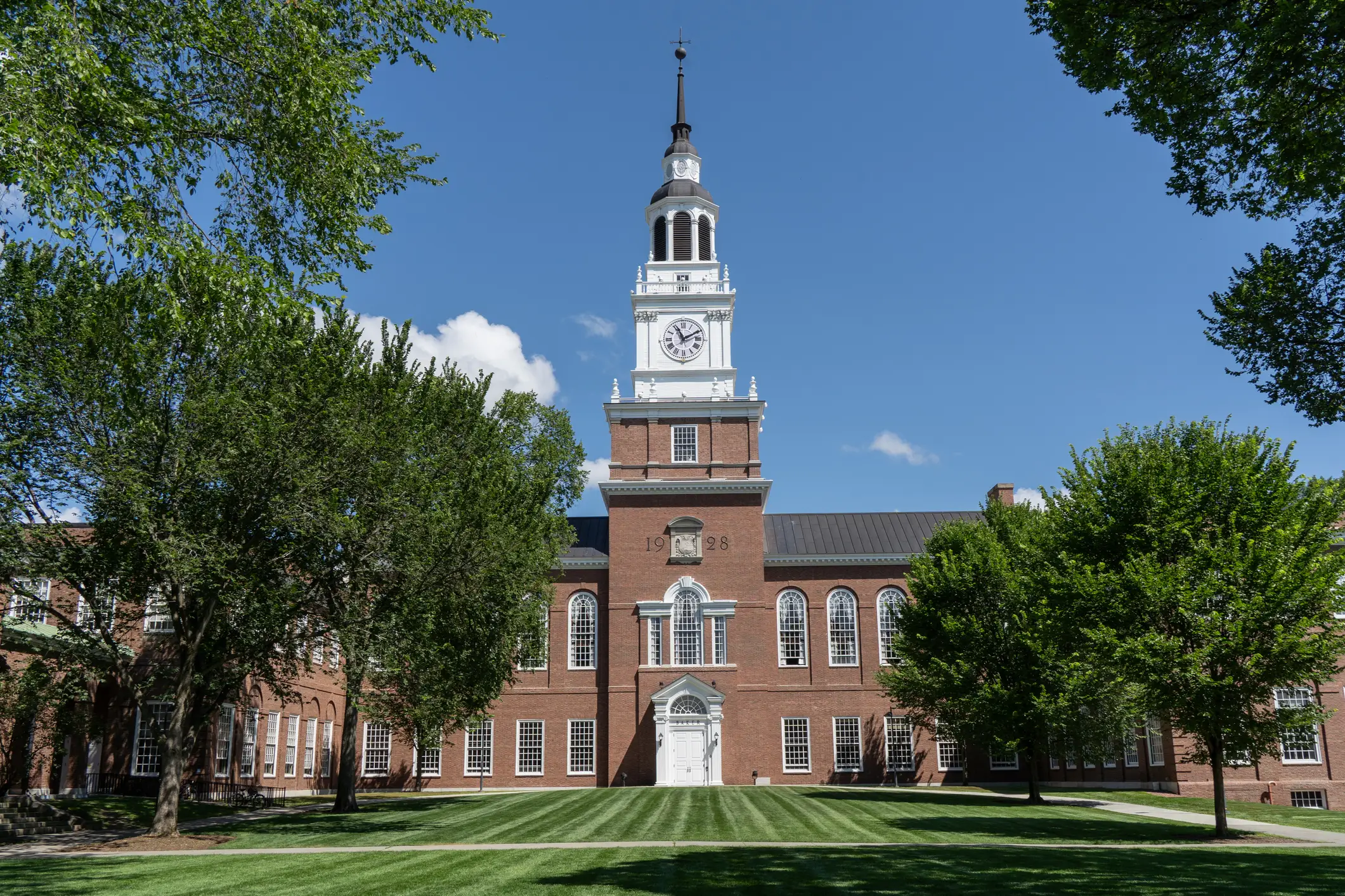 Baker-Berry Library’s clock tower rises above a brick campus building framed by trees and lawn.