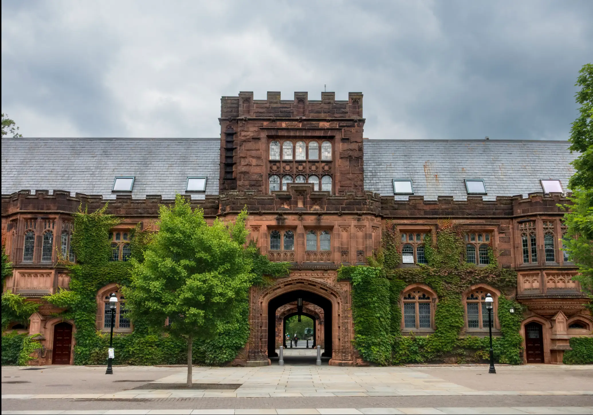 Ivy-covered Gothic stone campus building with an arched passageway beneath a cloudy sky.