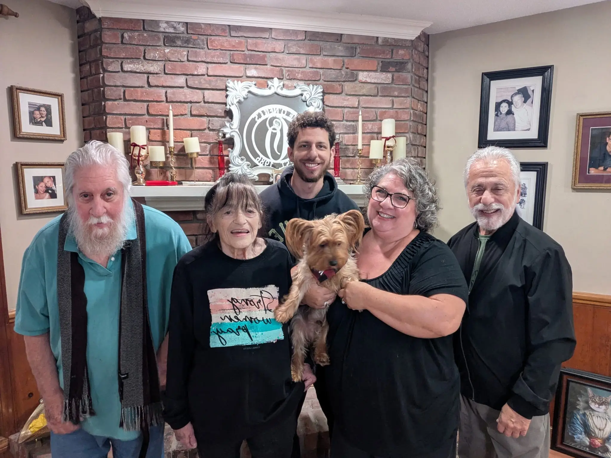 A family of five standing in front of a fireplace wth a dog.